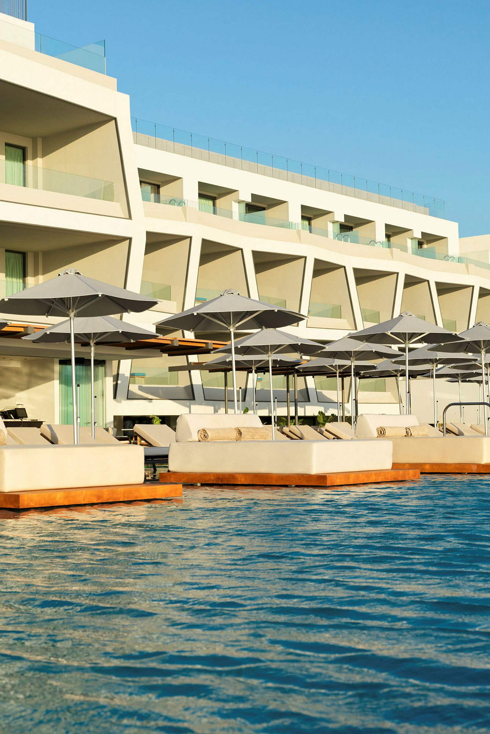 Liggestole og parasoller ved en pool foran et moderne hotel. (AI-genereret tekst)