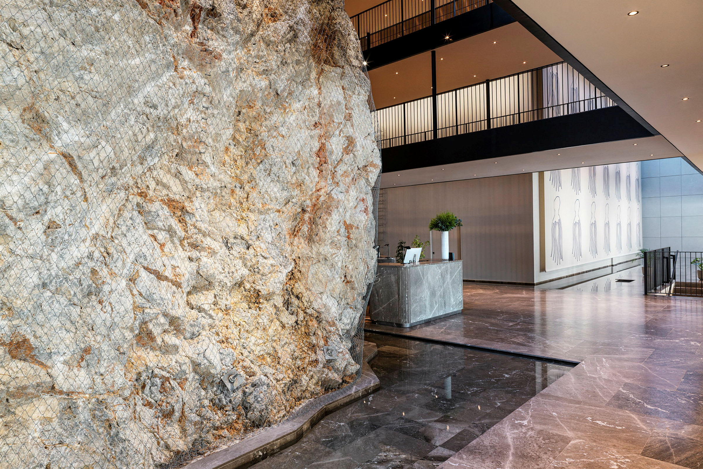 Billedet viser en hotelreception med en stor, naturlig klippevæg som en del af interiøret. (AI-genereret tekst)
