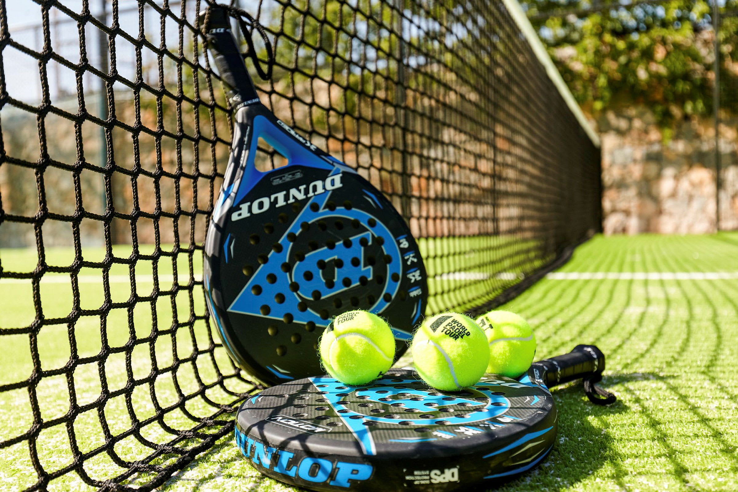 En padel ketsjer og padelbolde ved nettet på en padelbane. (AI-genereret tekst)