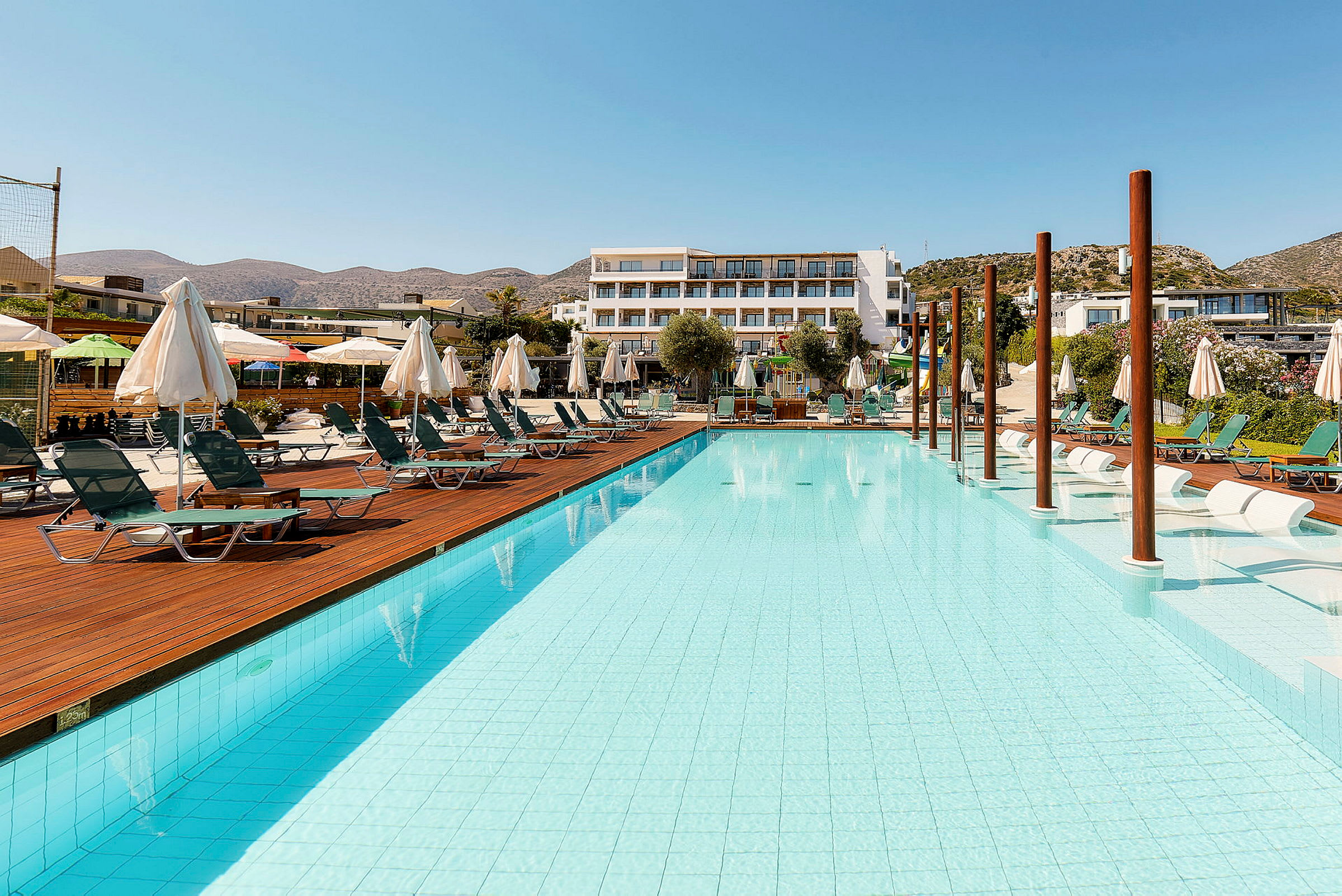 Poolområde med liggestole og parasoller ved siden af et hotel. (AI-genereret tekst)