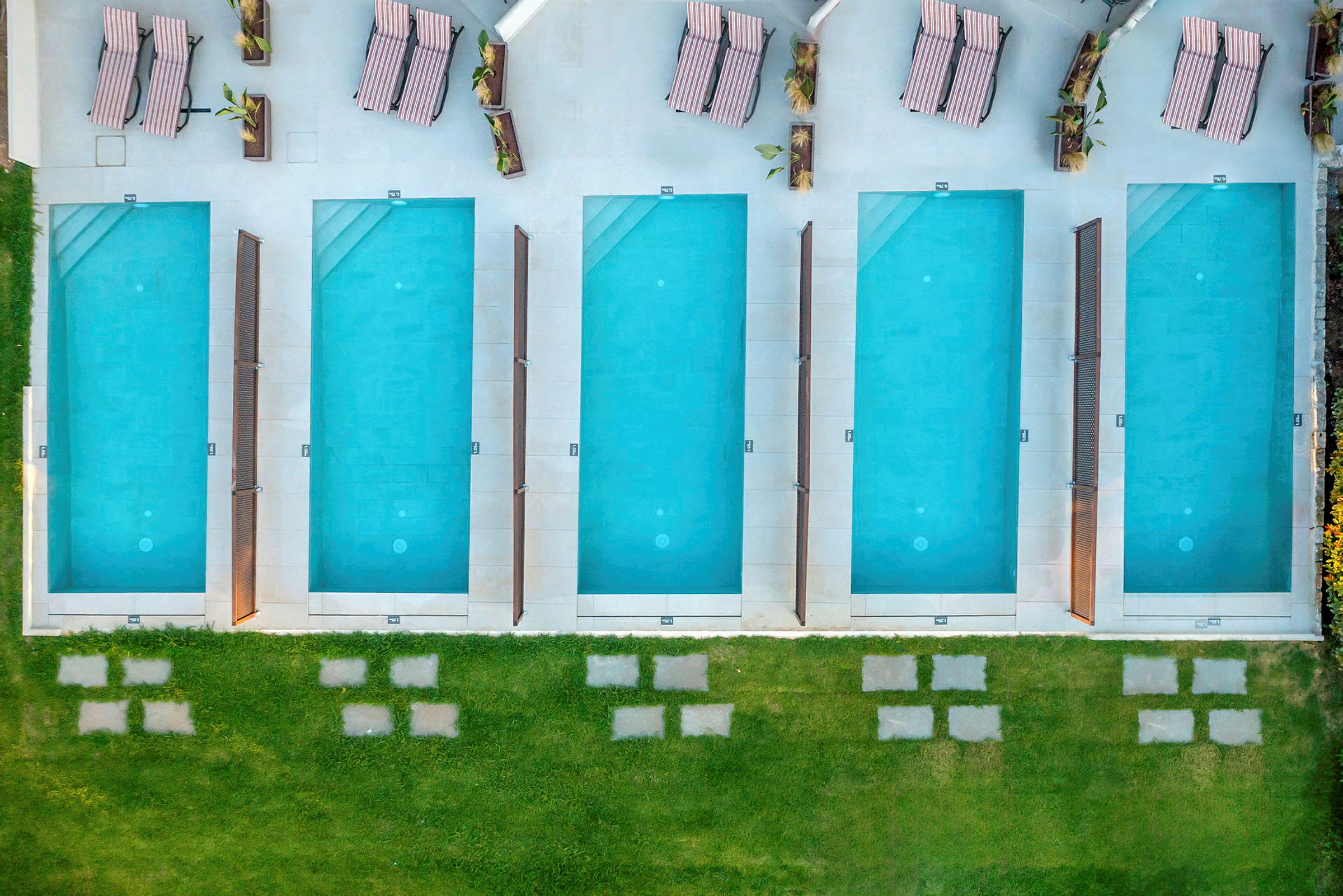 En række rektangulære pools og solsenge set oppefra. (AI-genereret tekst)