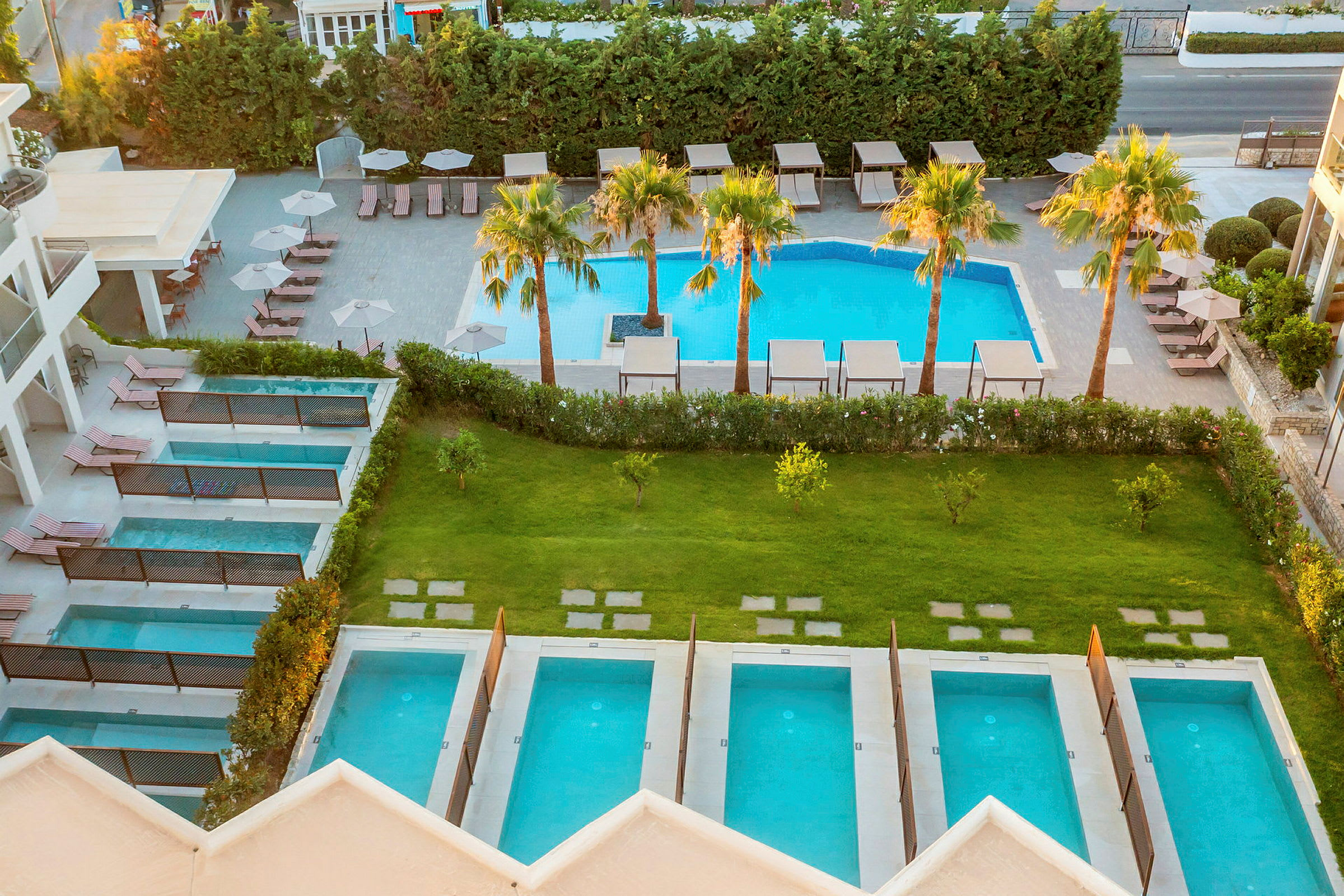 Udsigt over et hotelområde med flere private små pools og en større pool omgivet af liggestole og parasoller. (AI-genereret tekst)