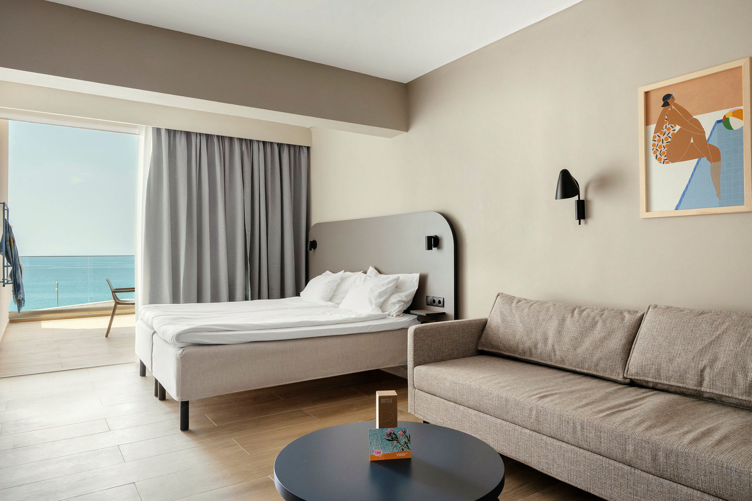 Et deluxe hotelværelse med lys indretning, en behagelig sofa, bord og en seng med udsigt over havet. (AI-genereret tekst)