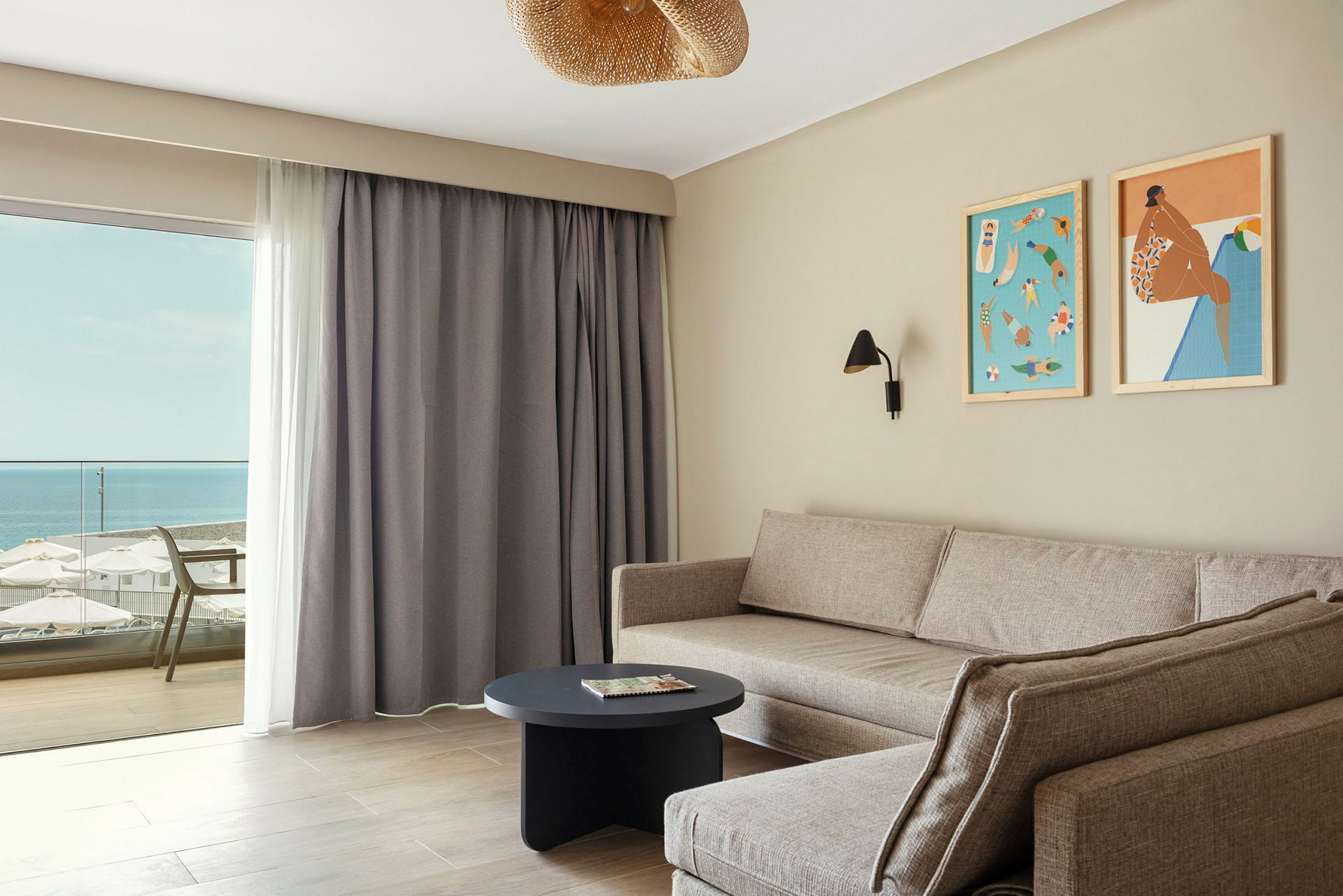 Stue med en komfortabel grå sofa og et rundt sofabord. En balkon med havudsigt ses gennem glasdøren. (AI-genereret tekst)