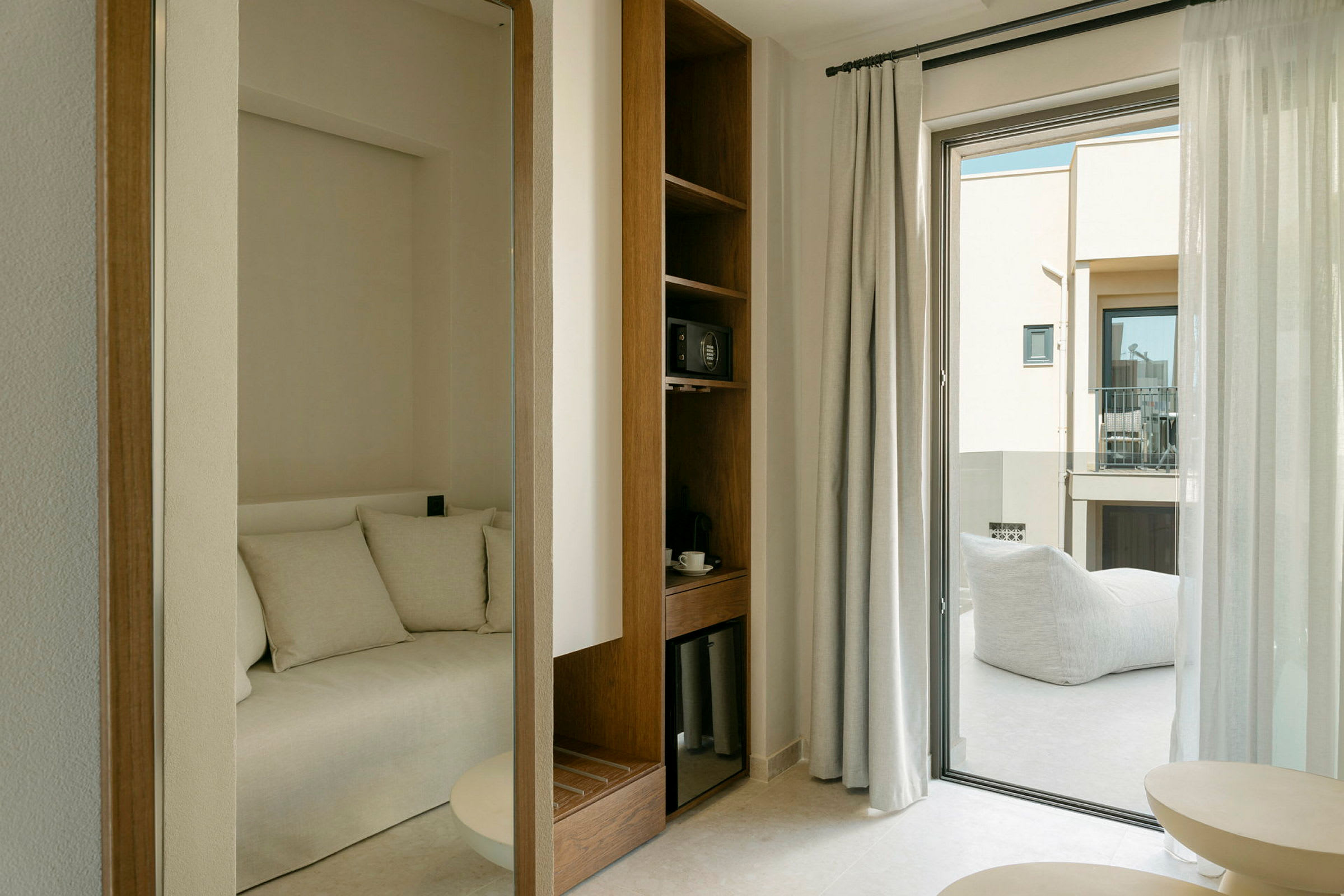 Et lyst hotelværelse med siddegruppe, hylde med genstande og balkon. (AI-genereret tekst)
