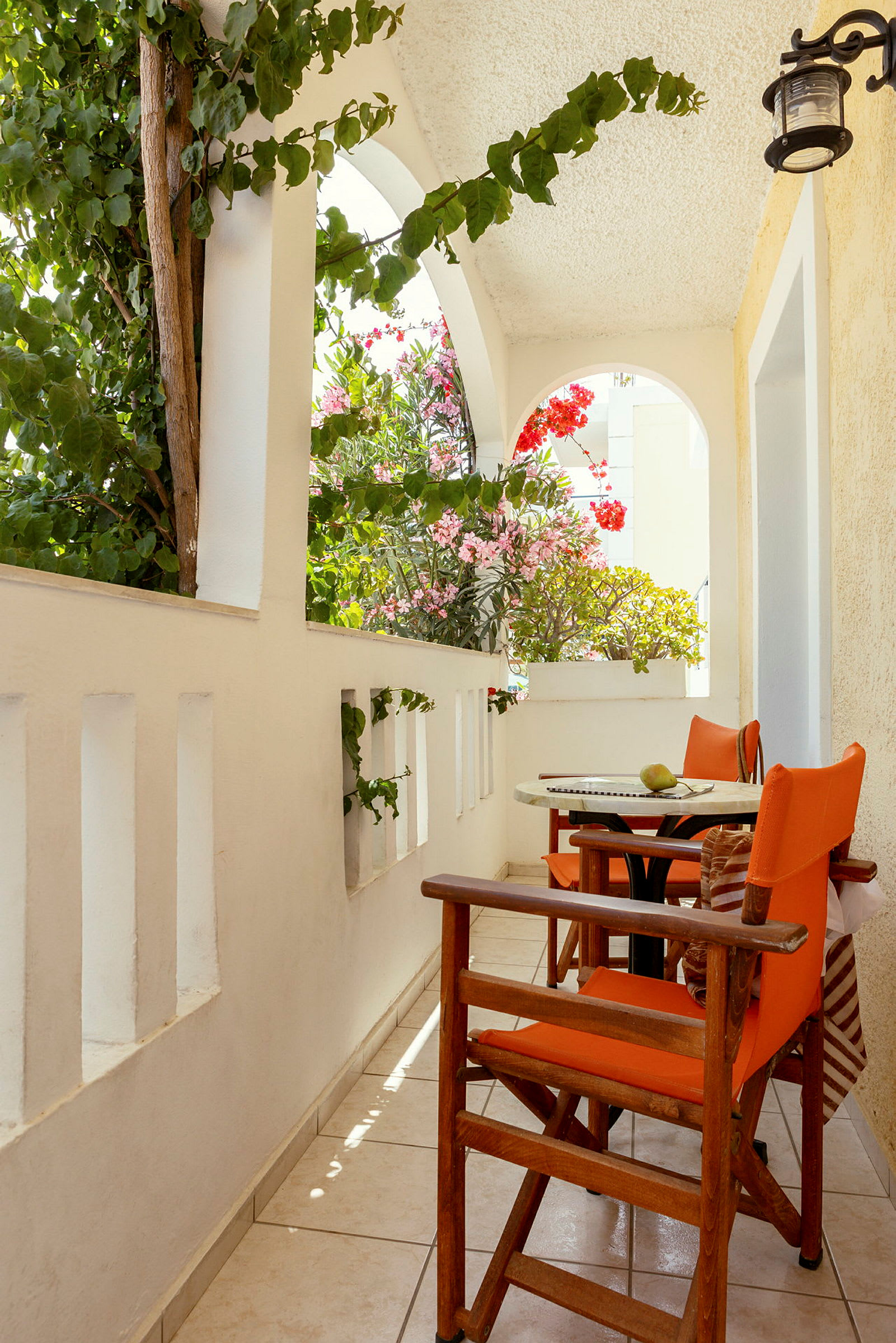 En terrasse med to orange stole ved et rundt bord. Dekorative planter i baggrunden. (AI-genereret tekst)