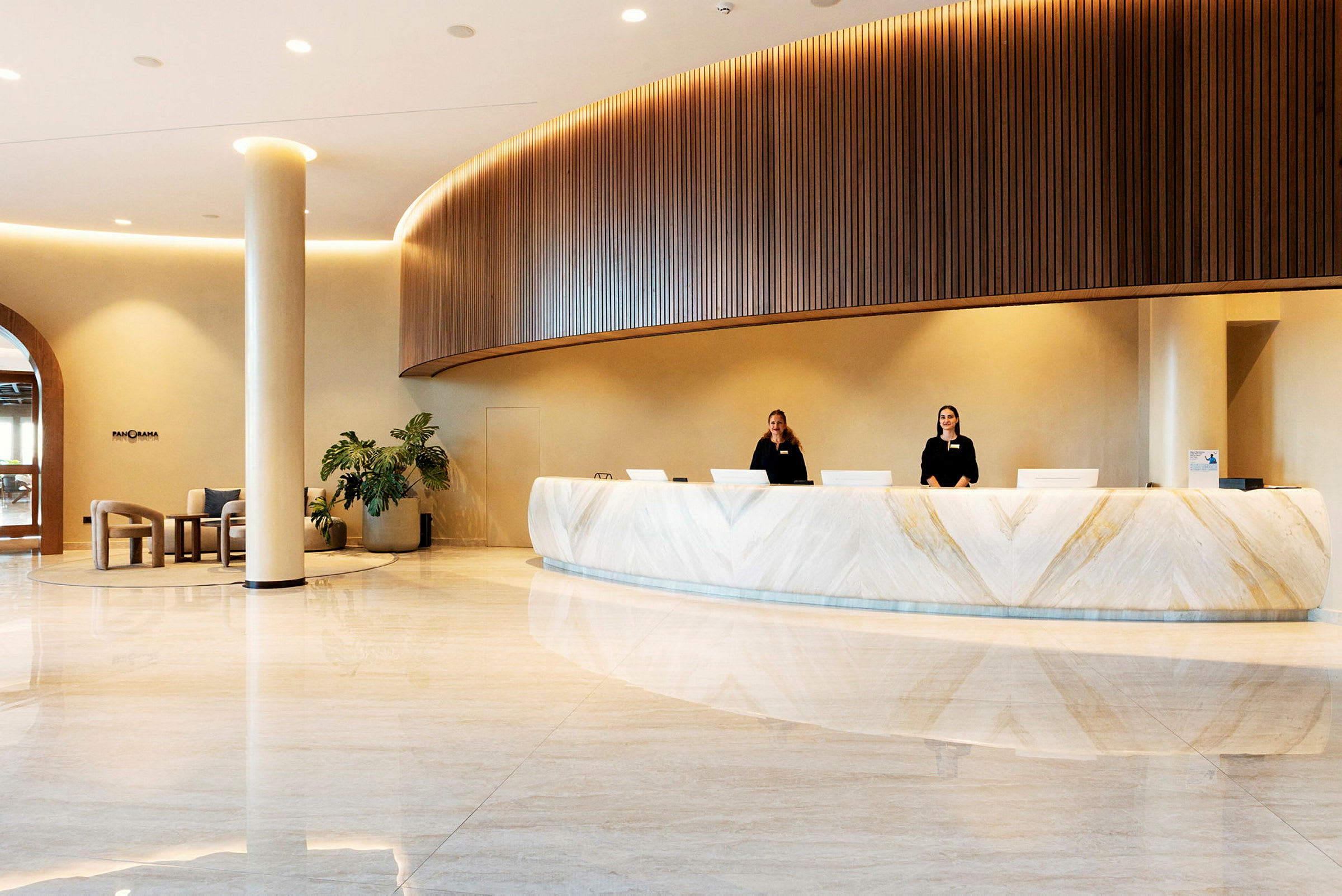 Billede af en hotelreception med moderne indretning, hvor to receptionister står bag en hvid marmoreret disk. (AI-genereret tekst)