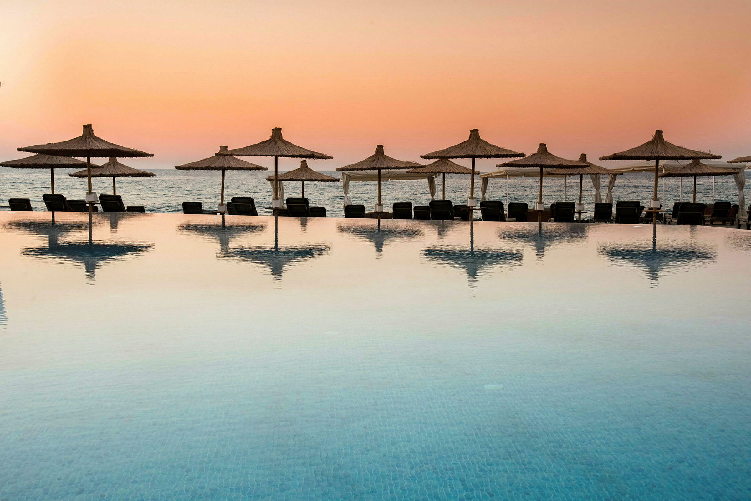 Pool med udsigt til stranden ved solnedgang. (AI-genereret tekst)