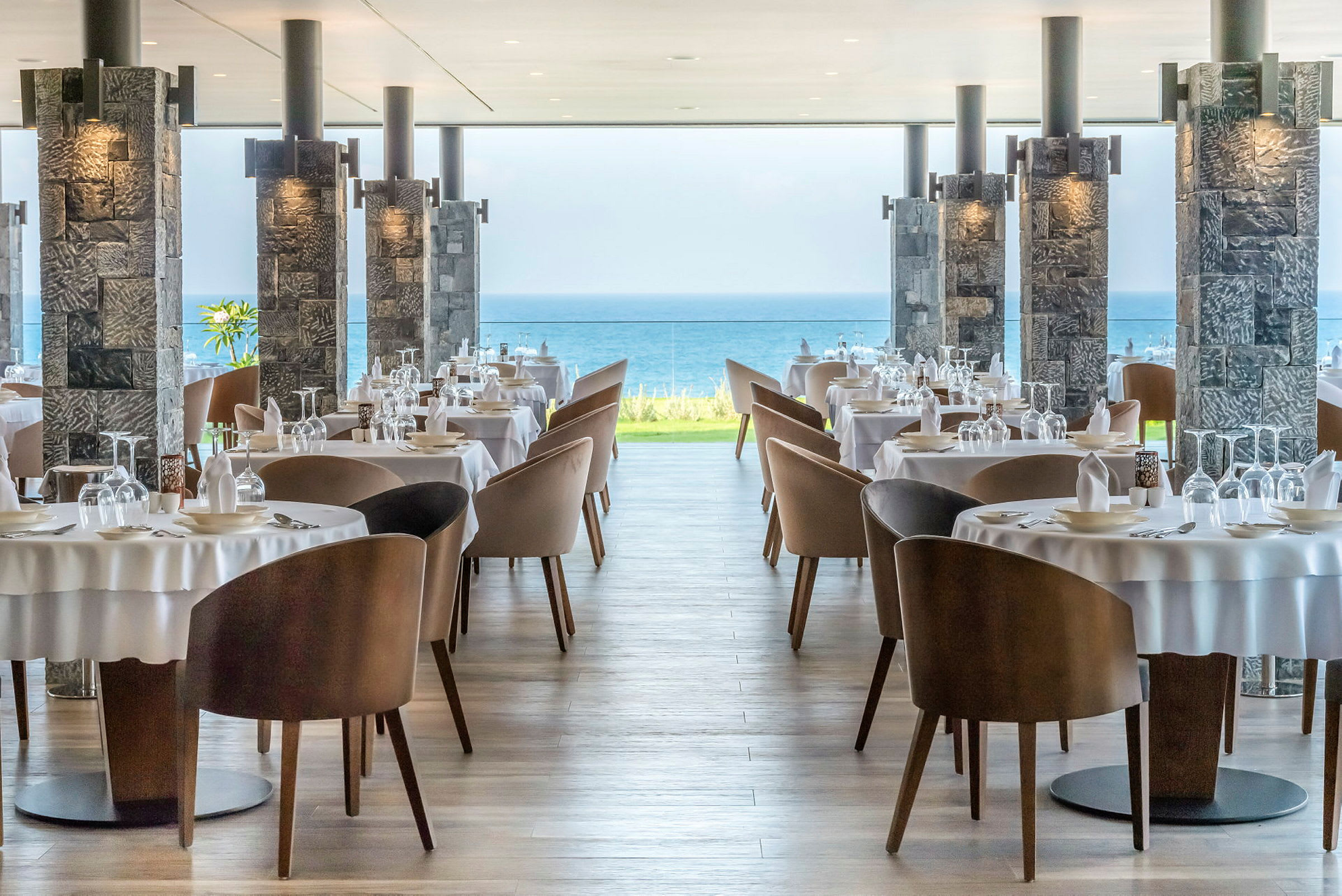 Restaurantborde med duge og stole, havudsigt i baggrunden. (AI-genereret tekst)