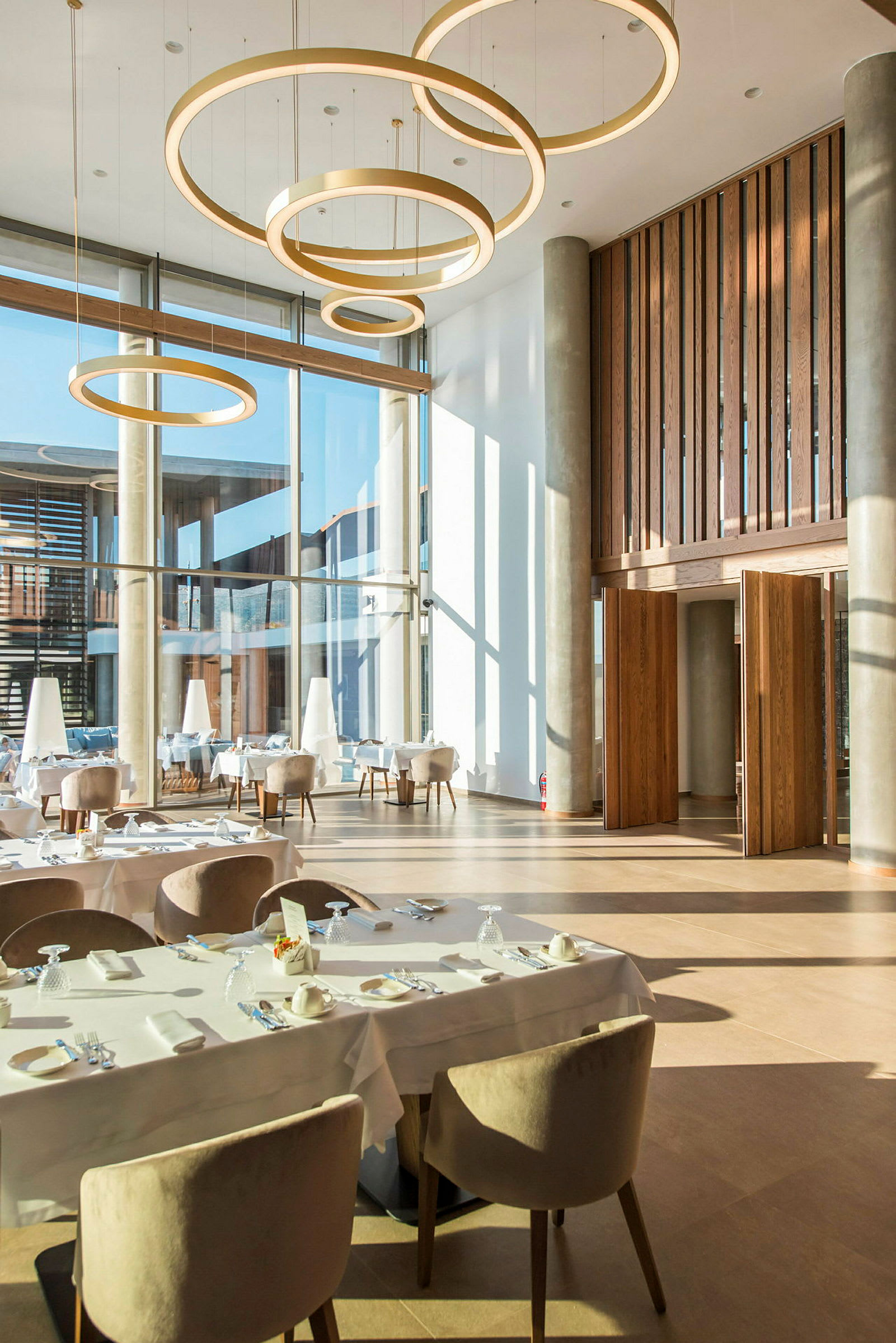 Interiør af en moderne restaurant med store vinduer og hængende cirkulære lamper. (AI-genereret tekst)