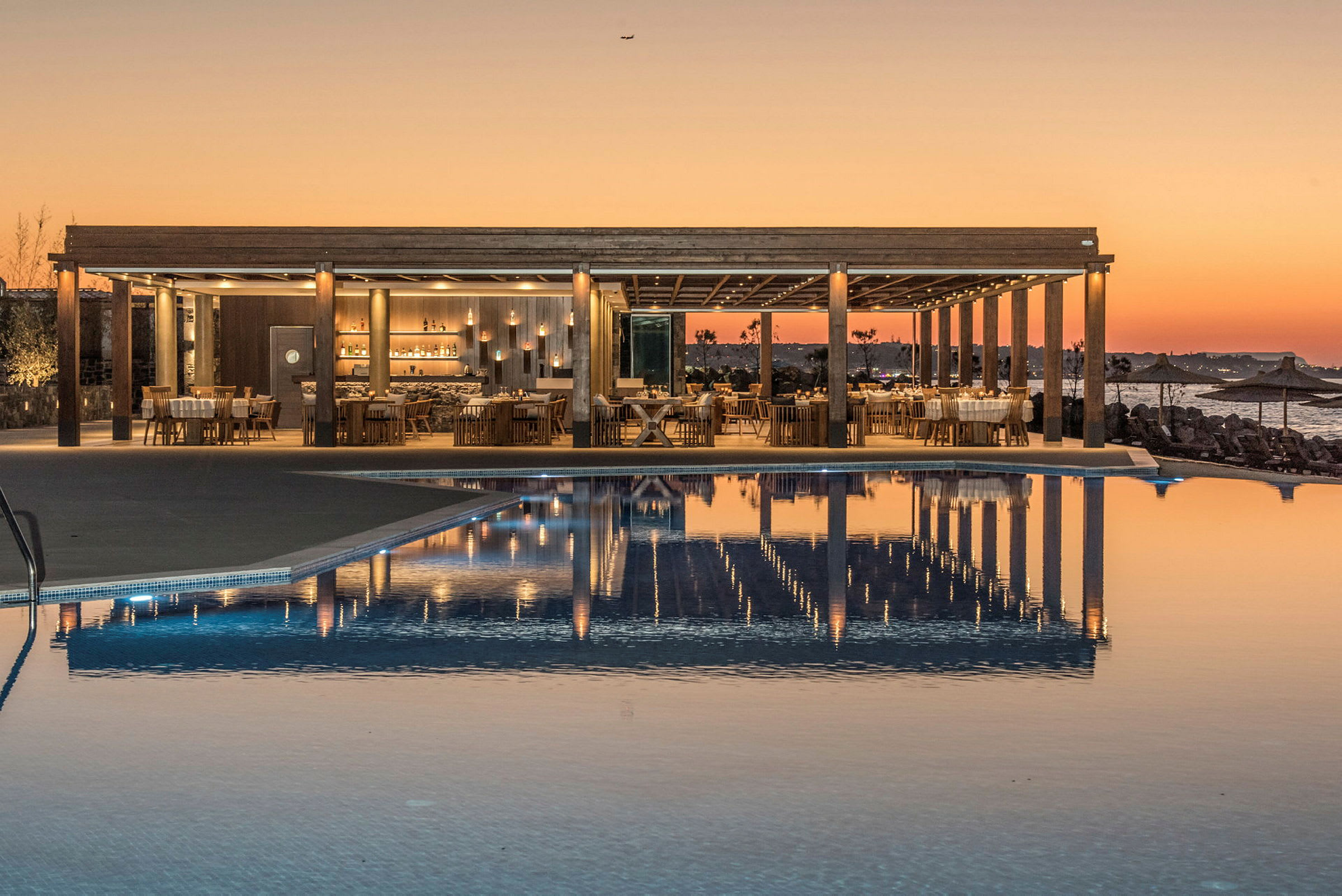 En restaurant ved en pool med solnedgang i baggrunden. (AI-genereret tekst)