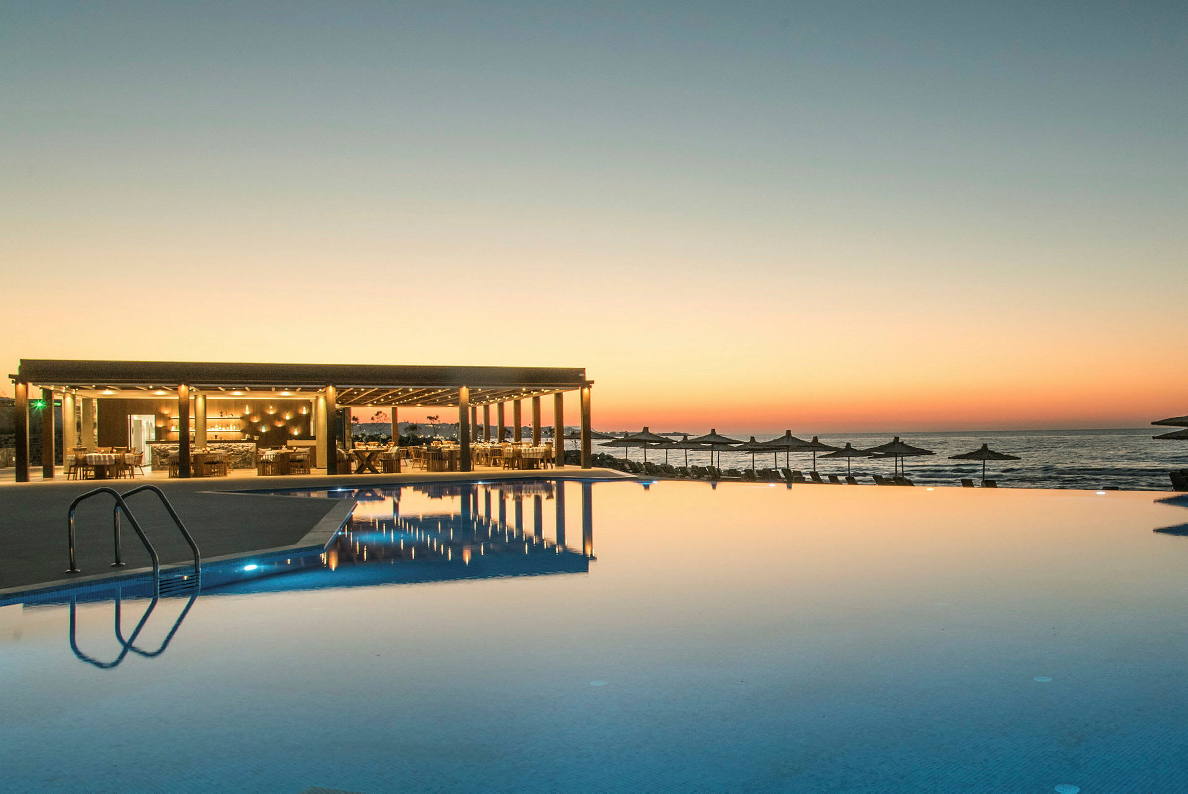 En infinitypool ved solnedgang med en restaurant til venstre og havet i baggrunden. (AI-genereret tekst)