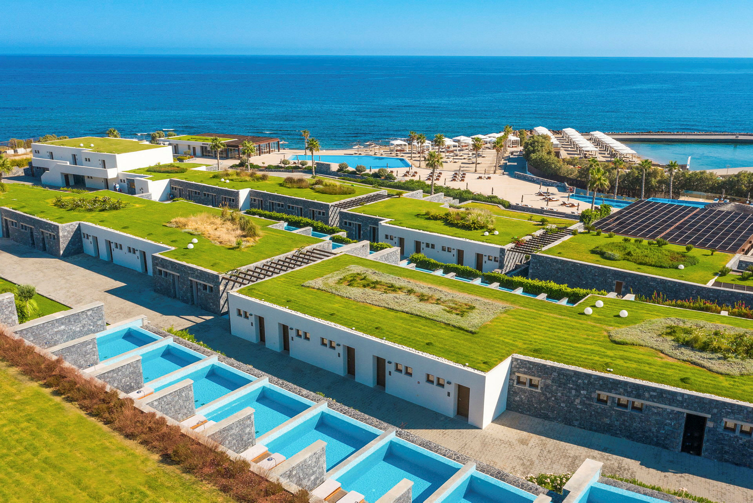 Billede af et hotelområde ved havet med grønne tage og private pools. (AI-genereret tekst)