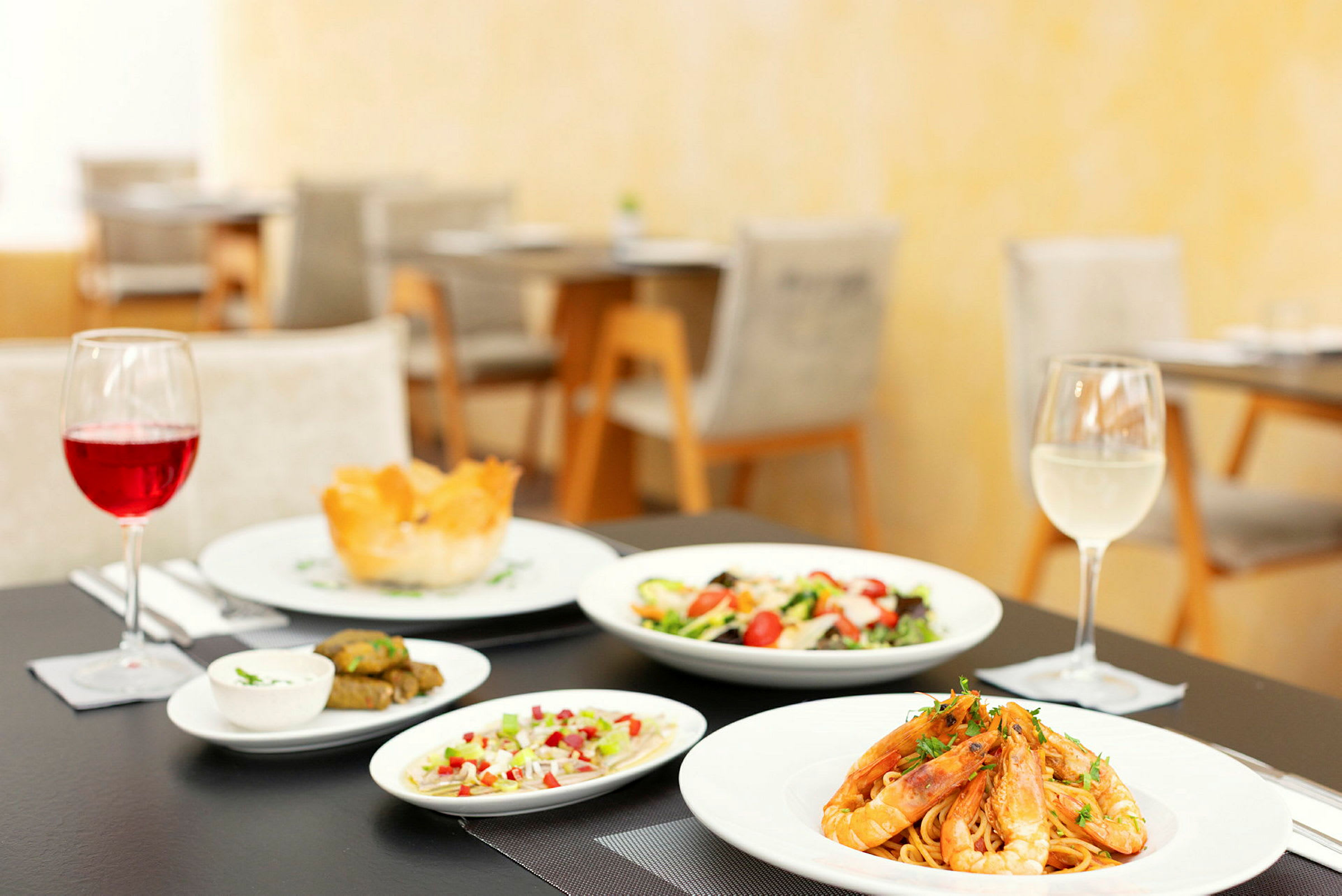 Billede af et dækket bord med et måltid, der inkluderer pasta med rejer, salat, småretter og to glas vin. (AI-genereret tekst)