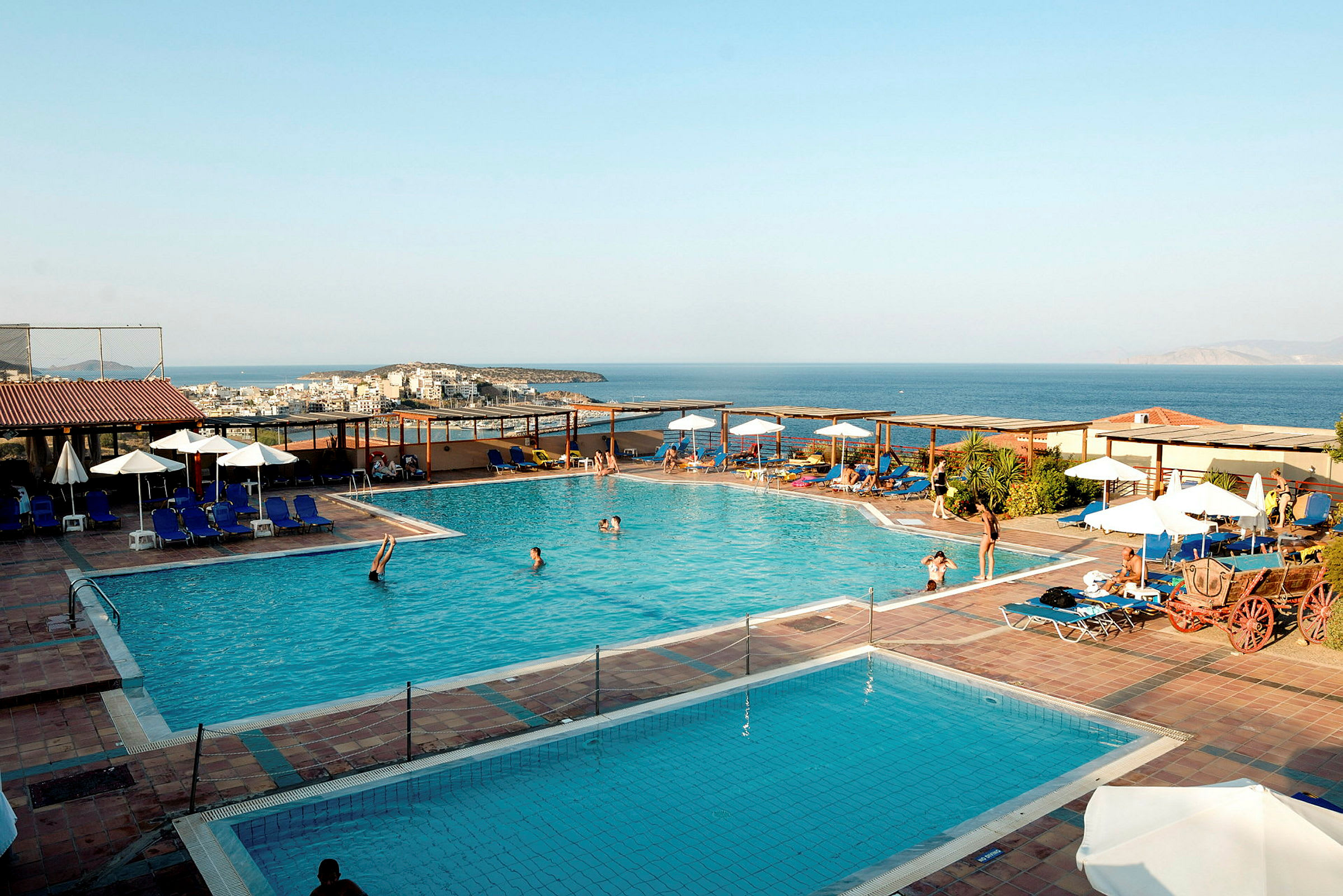 Udendørs swimmingpool ved et hotel med havudsigt i baggrunden. (AI-genereret tekst)