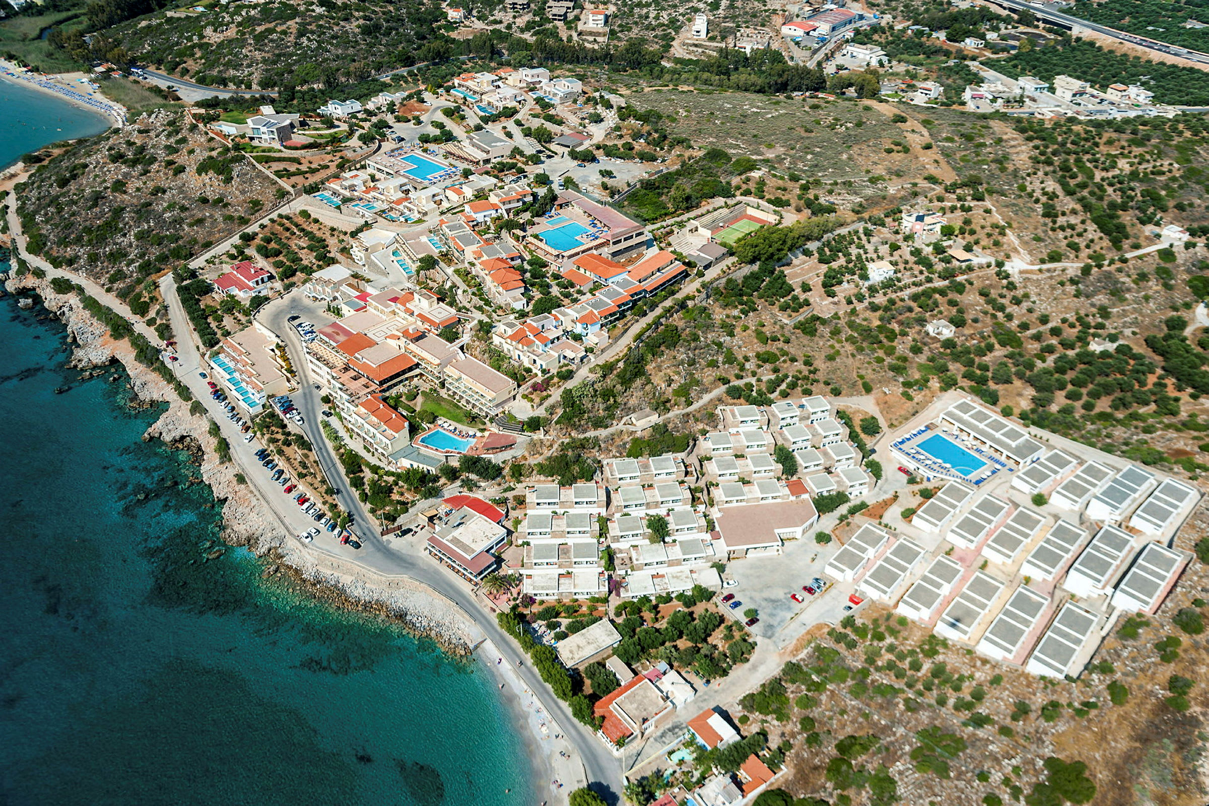 Luftfoto af en kystnær by med bygninger, hoteller og swimmingpools. (AI-genereret tekst)
