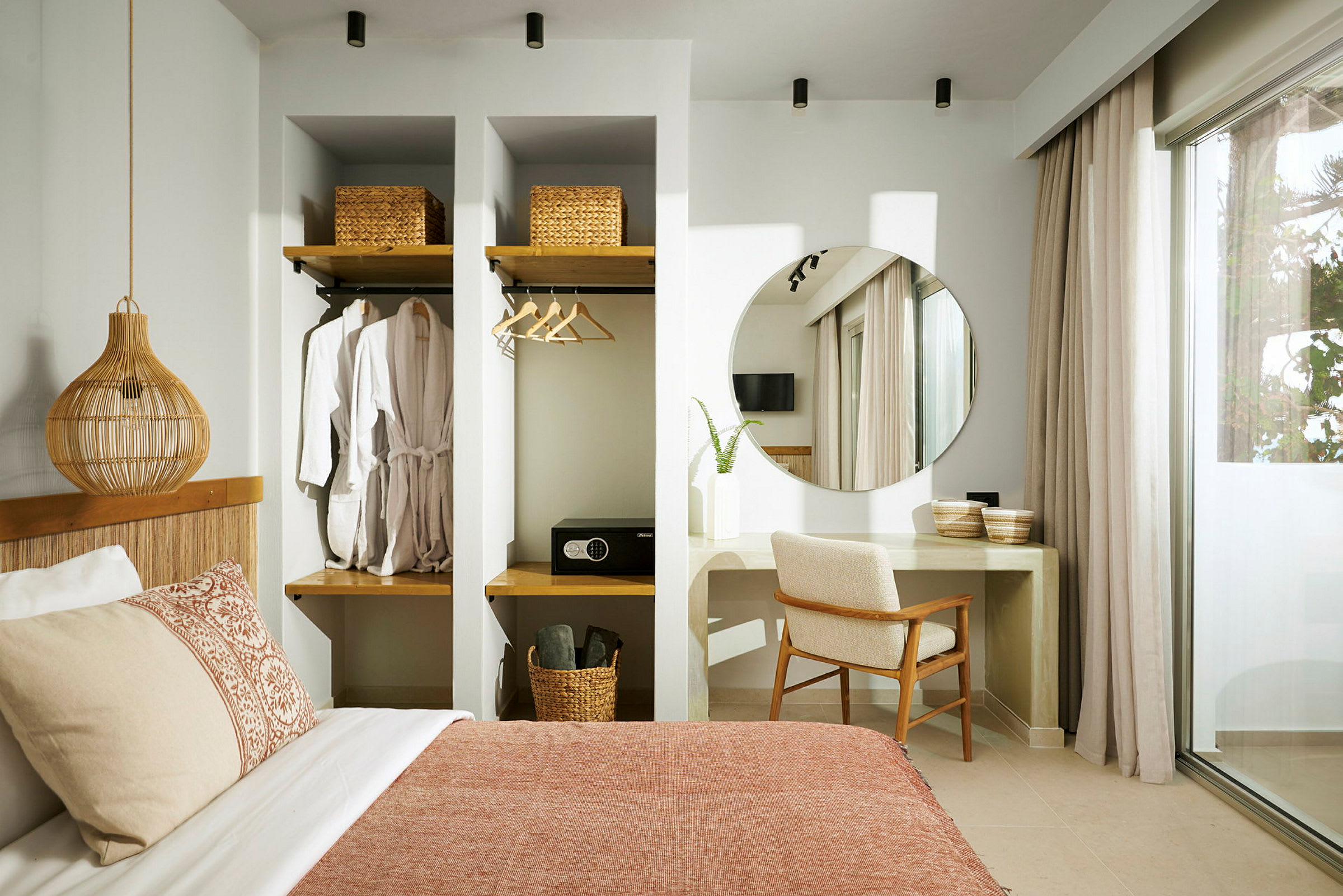 Indretning af et hotelværelse med seng, en vægmonteret garderobe, et skrivebord med spejl og stol samt store gardiner ved glasdøren. (AI-genereret tekst)