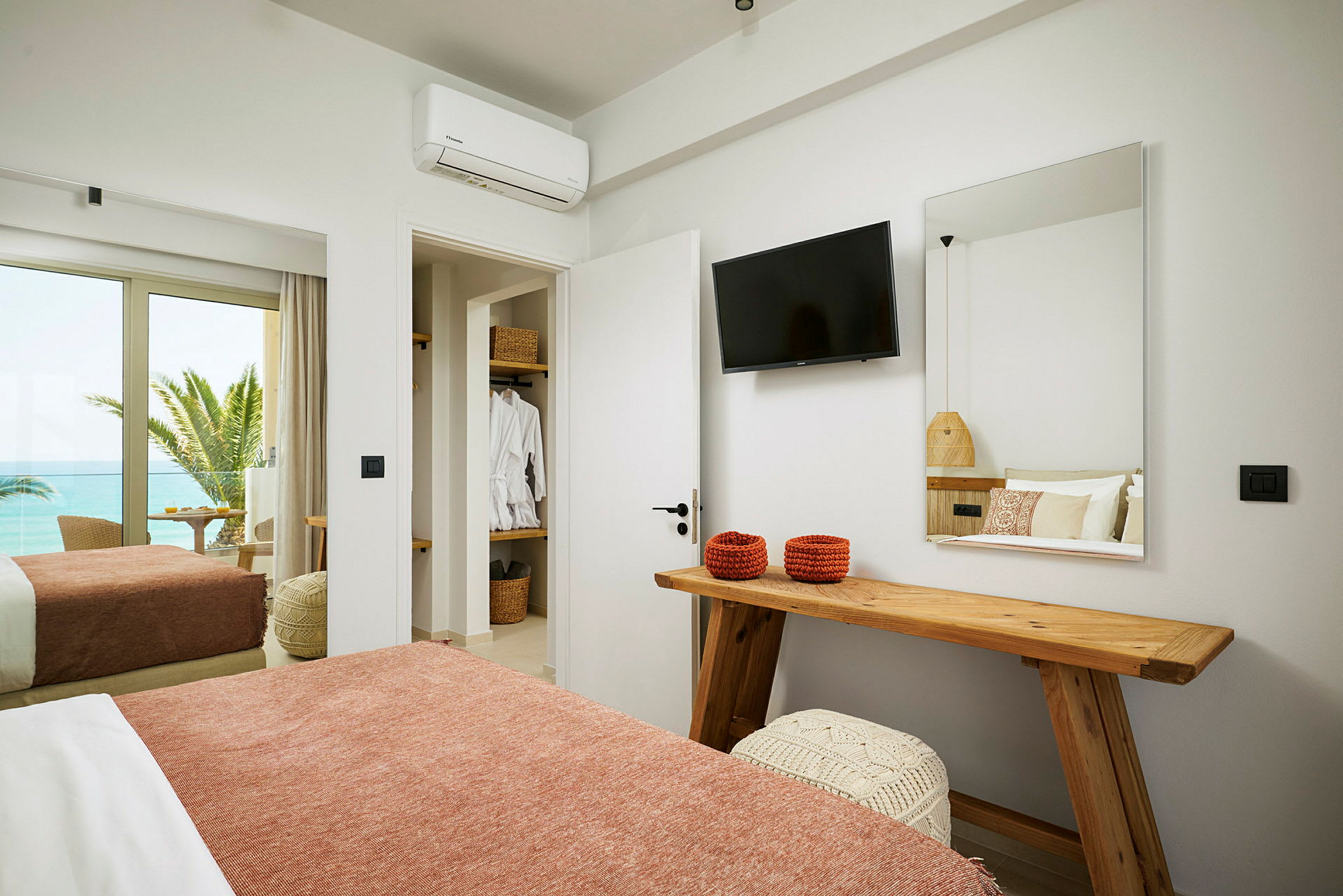 Hotelværelse med seng, TV, spejl og udsigt til havet. (AI-genereret tekst)