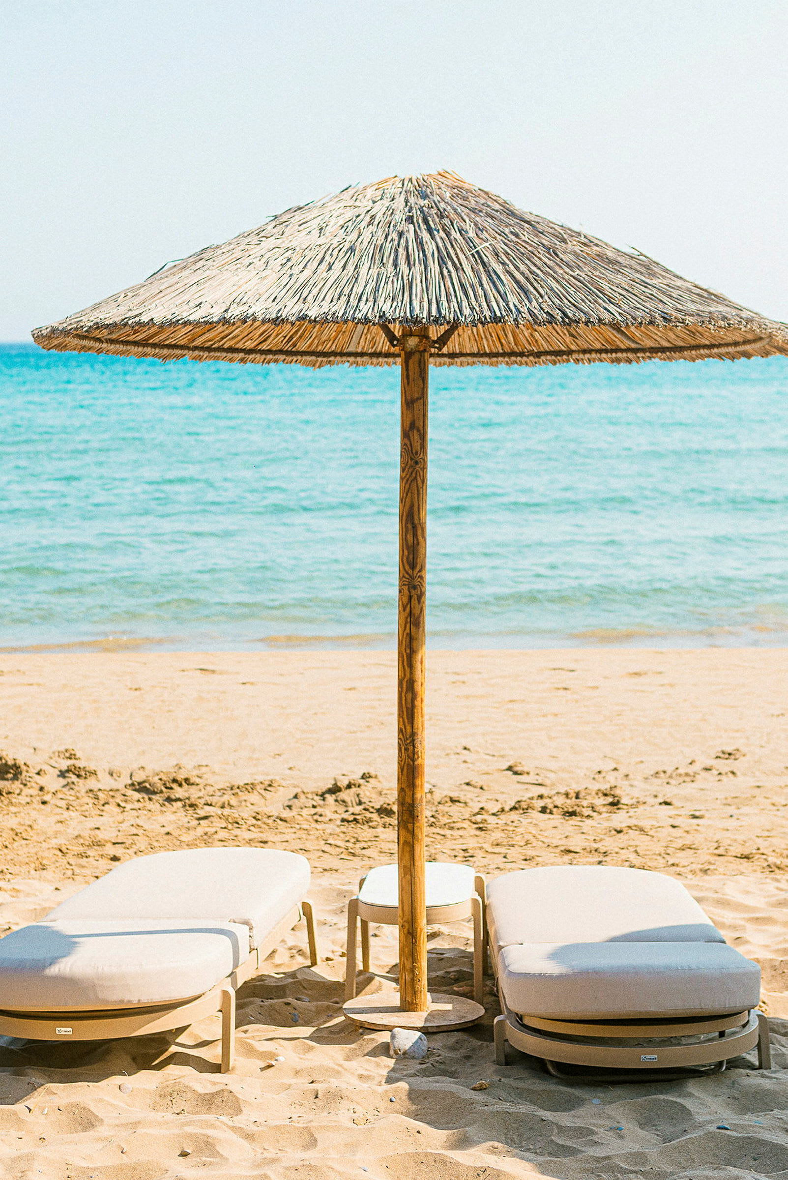 Strand med to liggestole og en parasol af strå. (AI-genereret tekst)