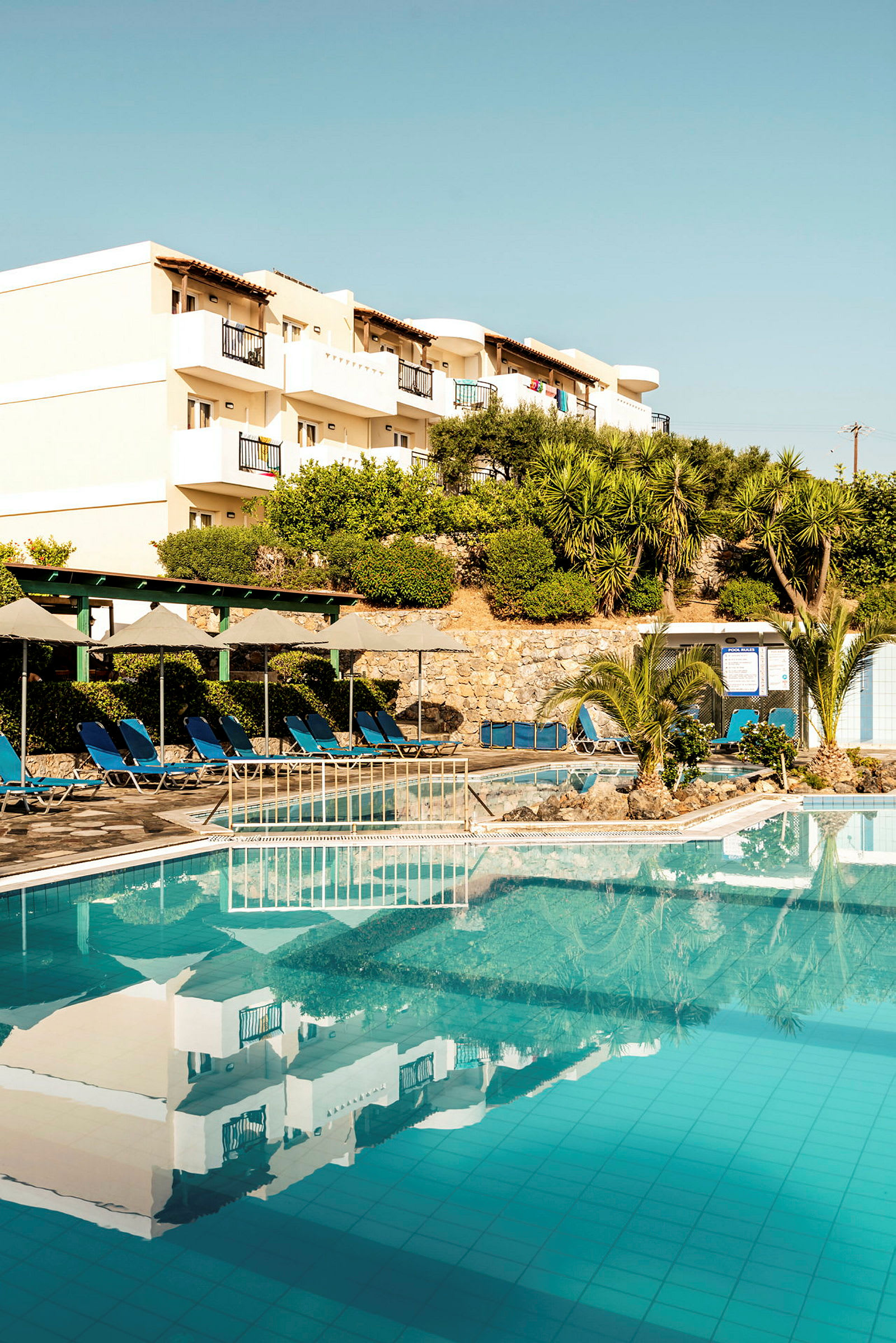 Et billede af en hotelpool med liggestole og bygninger i baggrunden. (AI-genereret tekst)