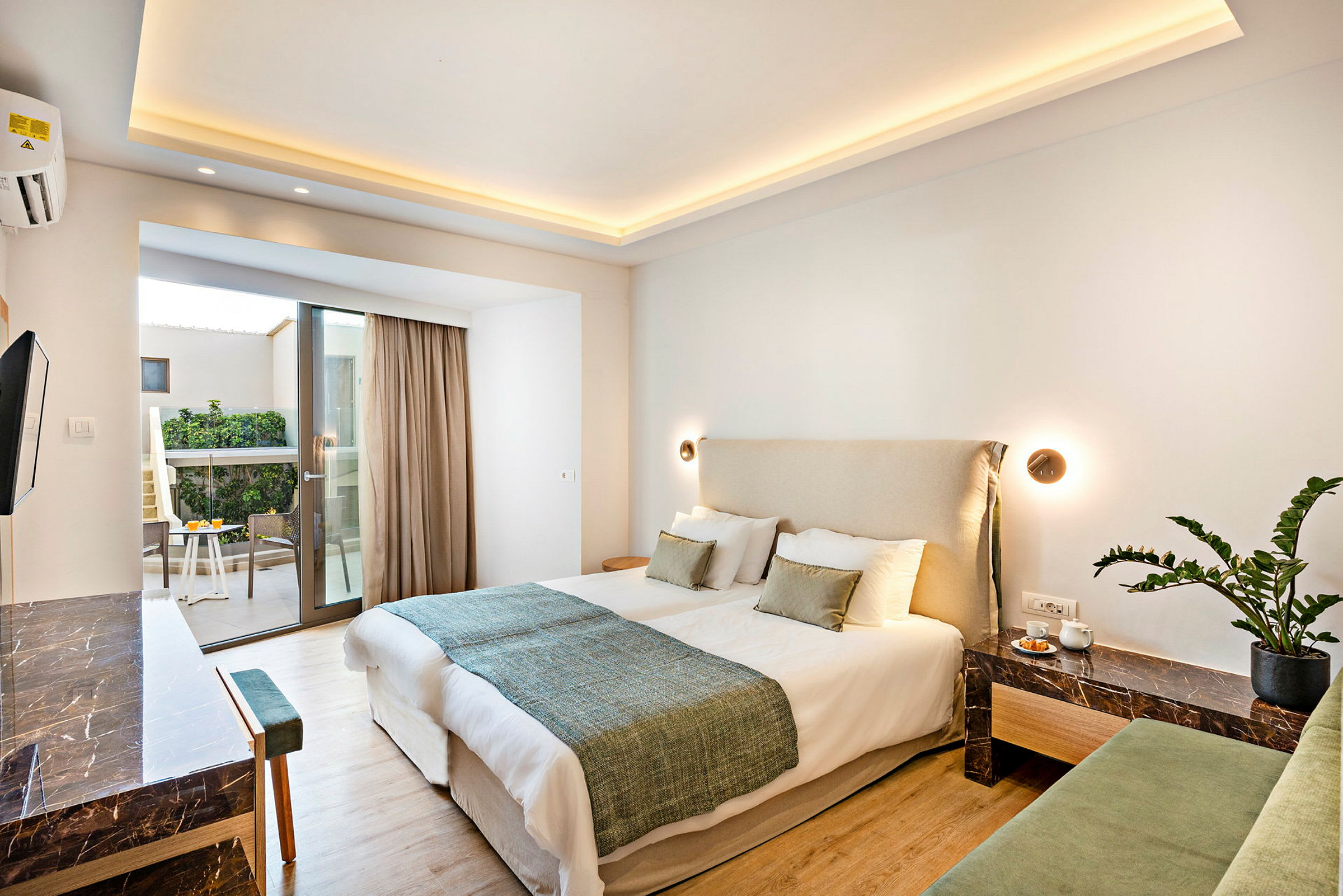 Et hotelværelse med en dobbeltseng, et sidebord med dekoration og en balkon med udsigt over en have. (AI-genereret tekst)