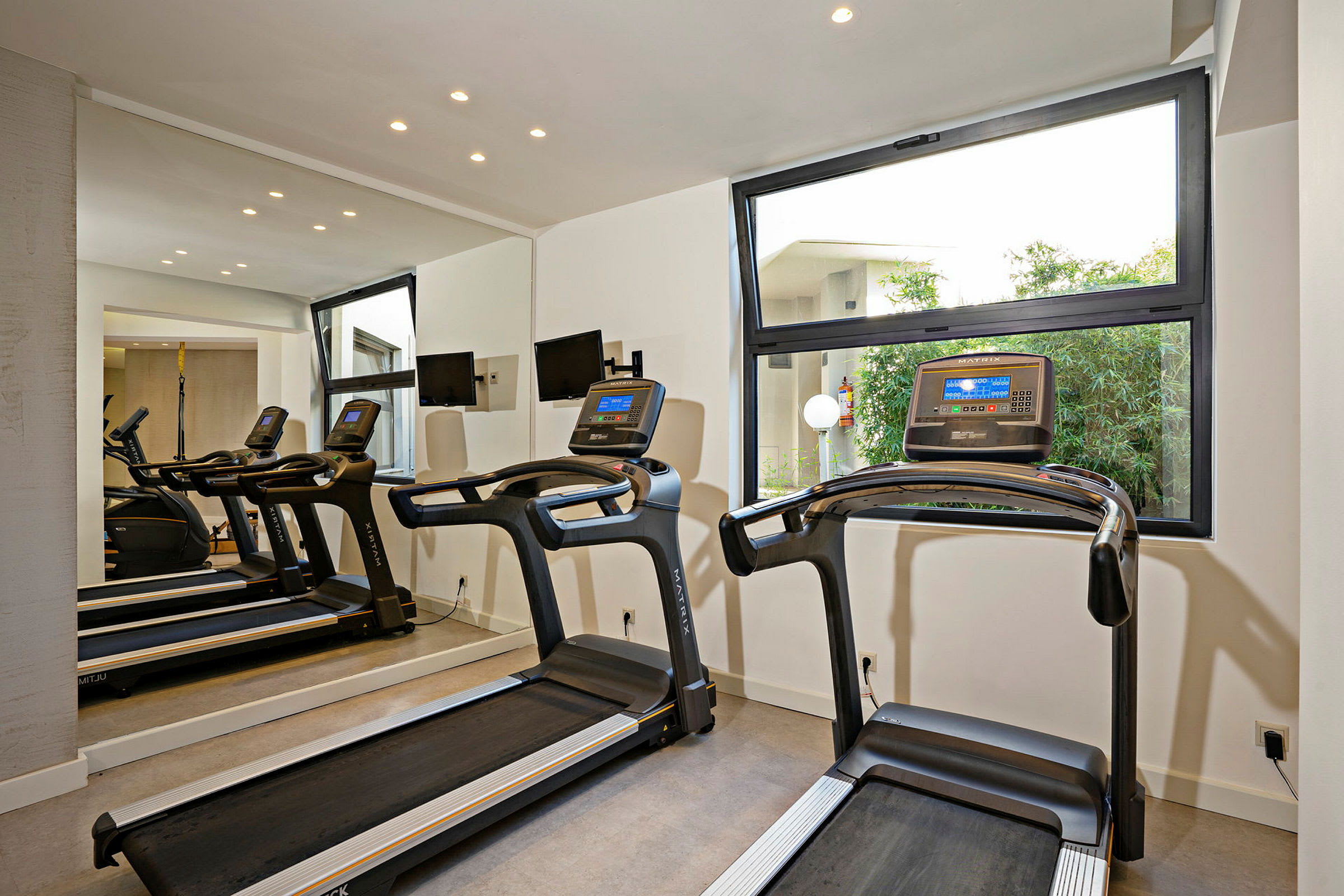 To løbebånd i et fitnesscenter med store vinduer. (AI-genereret tekst)