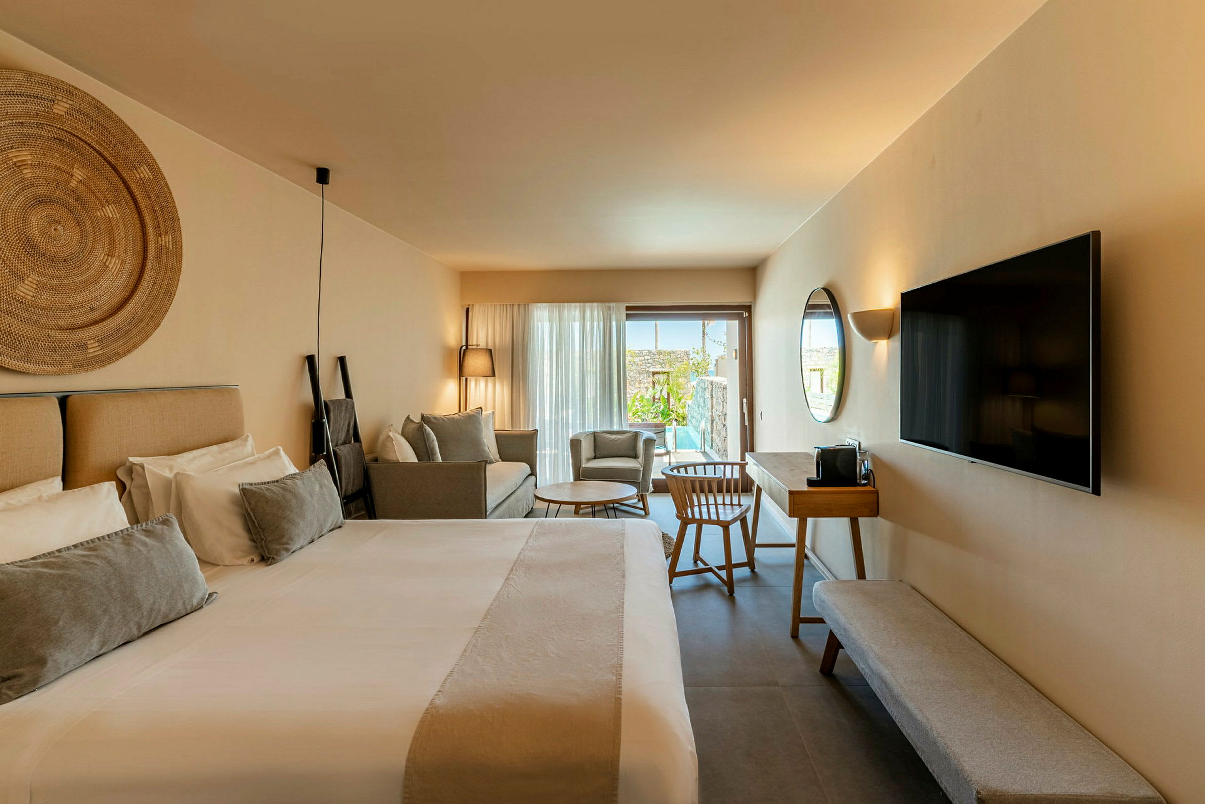 Et moderne hotelværelse med en stor seng, en sofa, et TV på væggen og et skrivebord med stol. Værelset har en terrasse med udsigt til poolen. (AI-genereret tekst)