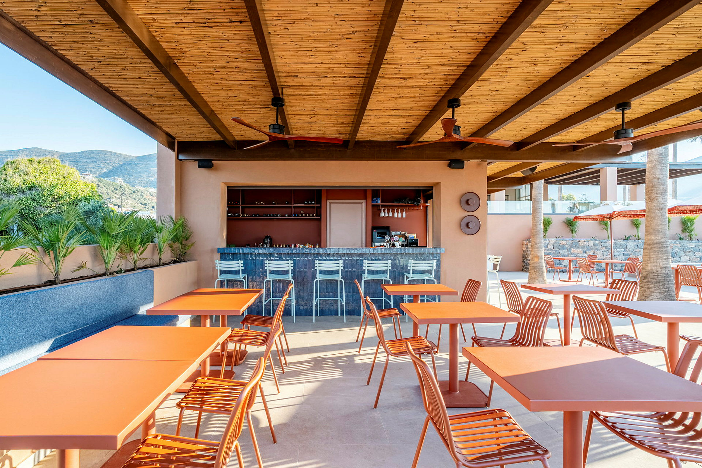 Restaurant eller bar med orange borde og stole under et tag i et udendørsmiljø. (AI-genereret tekst)