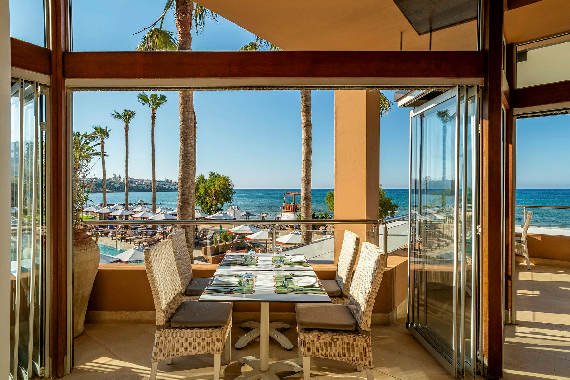 En udendørs restaurant med borde og stole, udsigt over stranden og havet i baggrunden. (AI-genereret tekst)