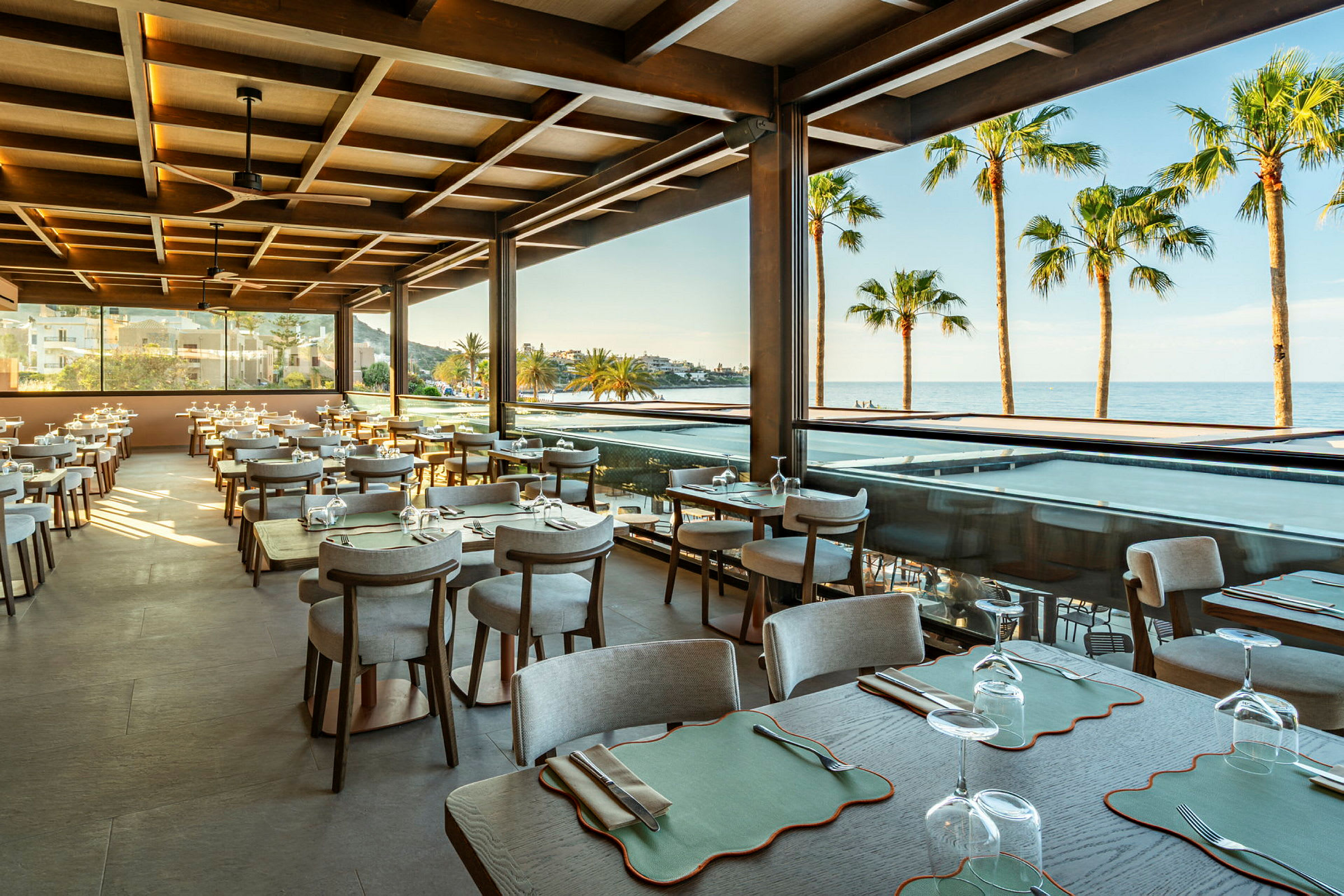 Restaurant med siddepladser, udsigt til havet og palmer. (AI-genereret tekst)