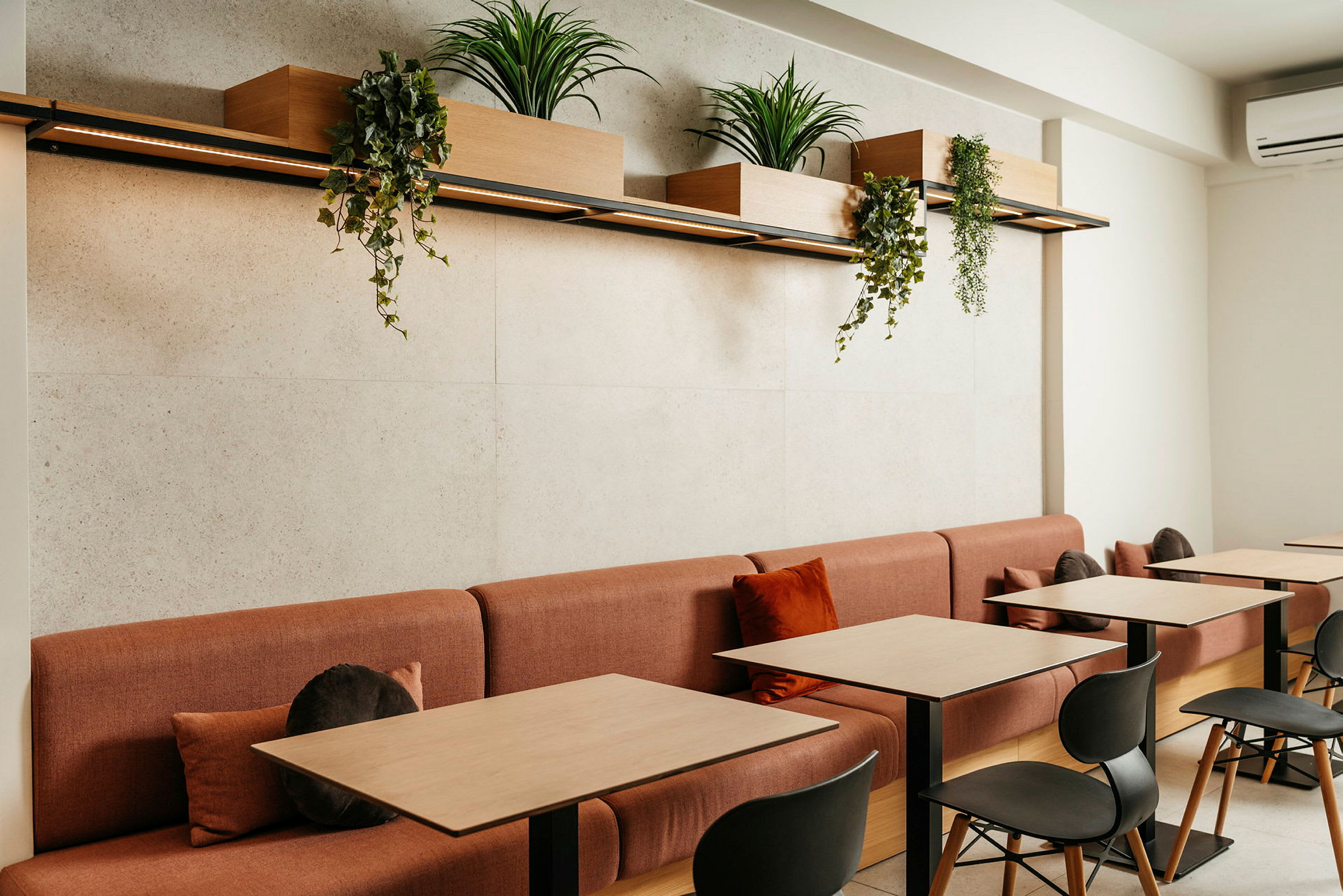 Et moderne caféområde med røde sofaer og træborde, dekoreret med plantekasser hængende ovenover. (AI-genereret tekst)