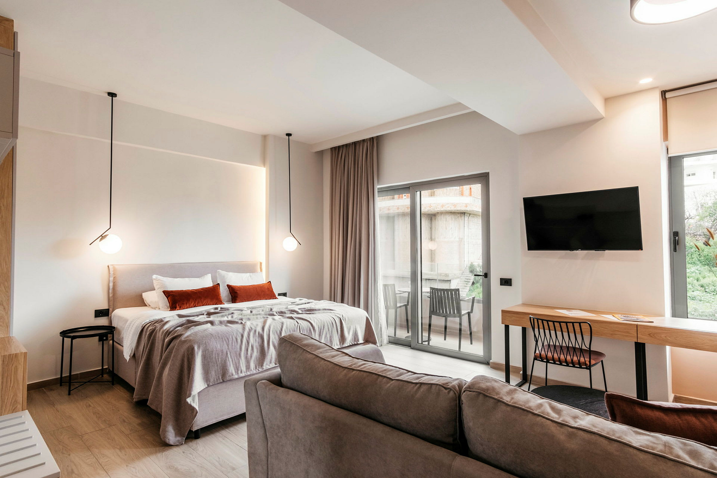 Et moderne hotelværelse med seng, sofa, skrivebord, TV og en balkon med udsigt. (AI-genereret tekst)