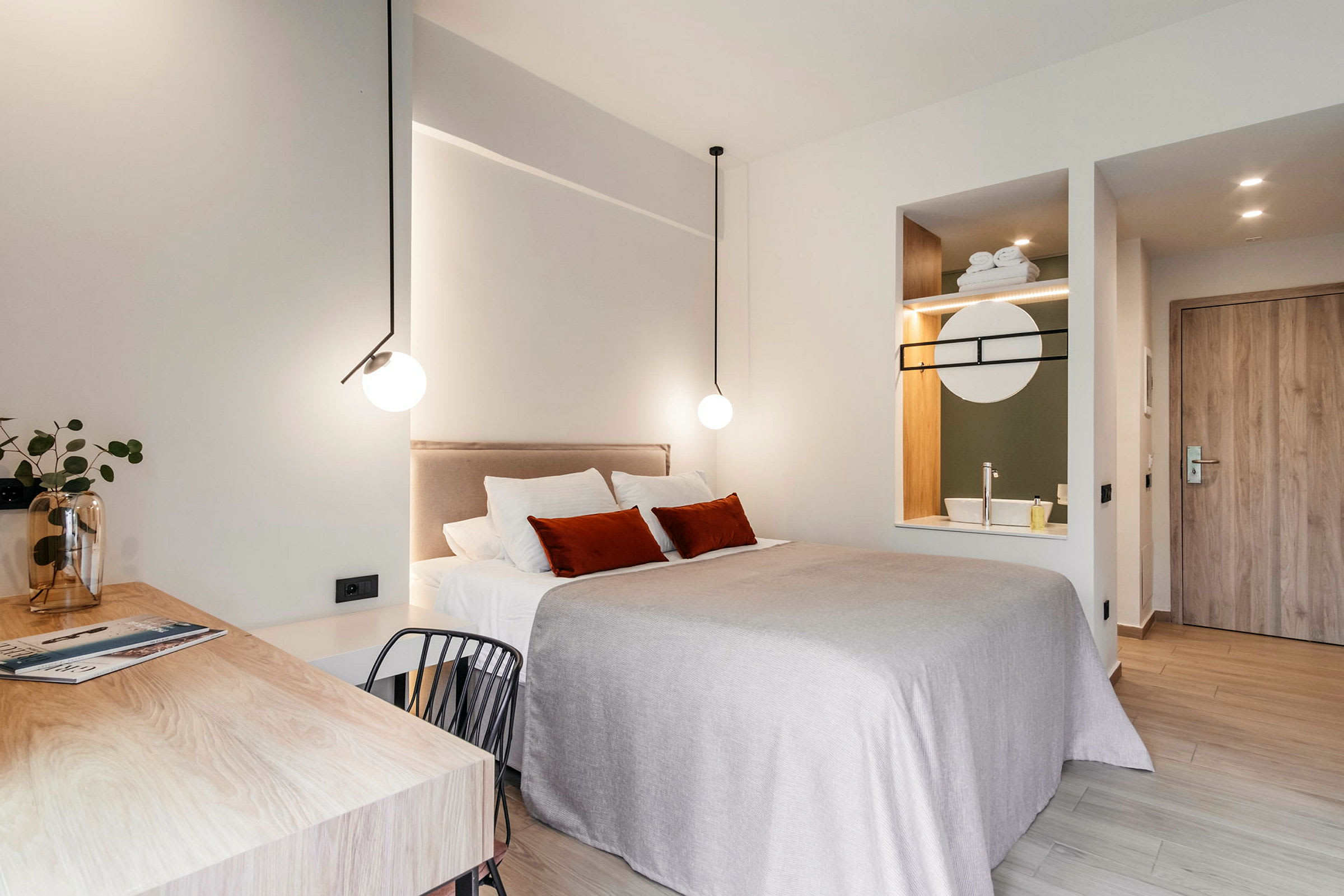 Et moderne indrettet hotelværelse med en dobbeltseng, skrivebord og integreret vask med spejl. (AI-genereret tekst)