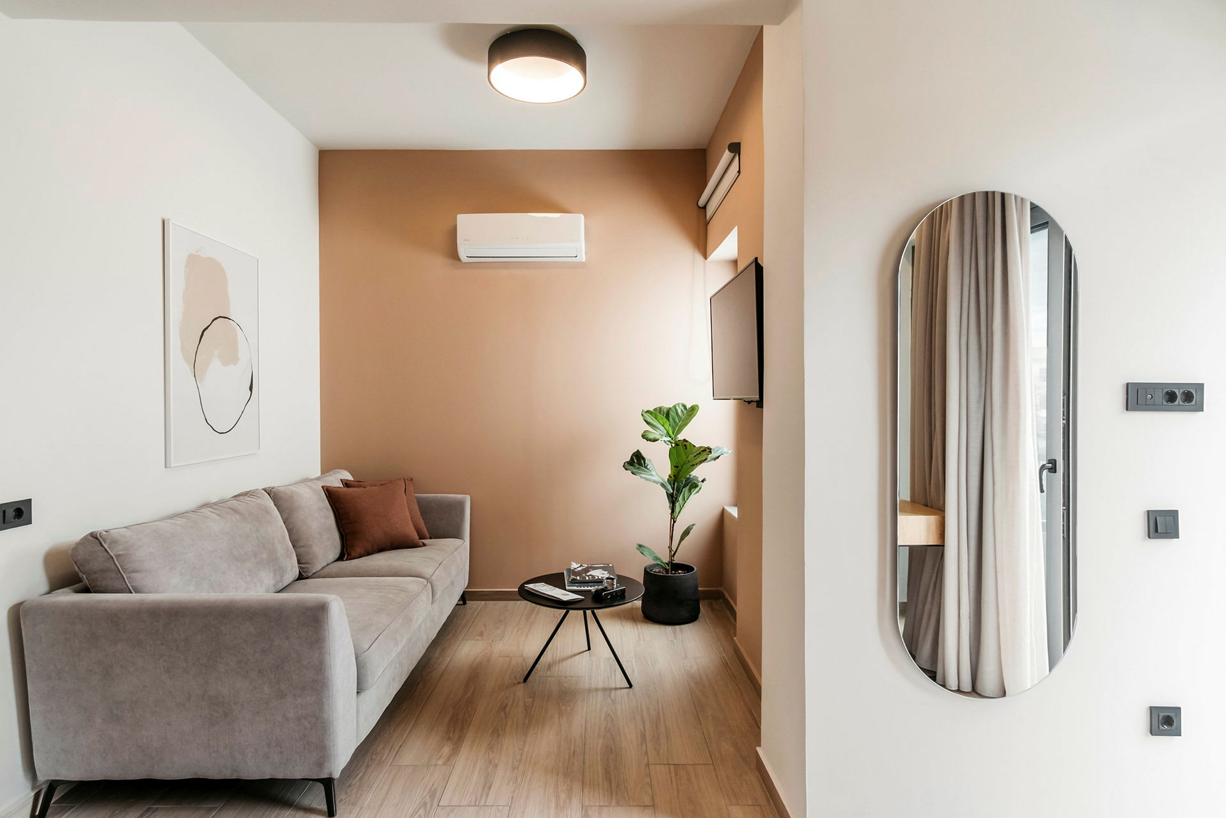 En moderne stue med en grå sofa, et lille rundt sofabord, en plante i krukke og et vægmonteret fjernsyn. (AI-genereret tekst)