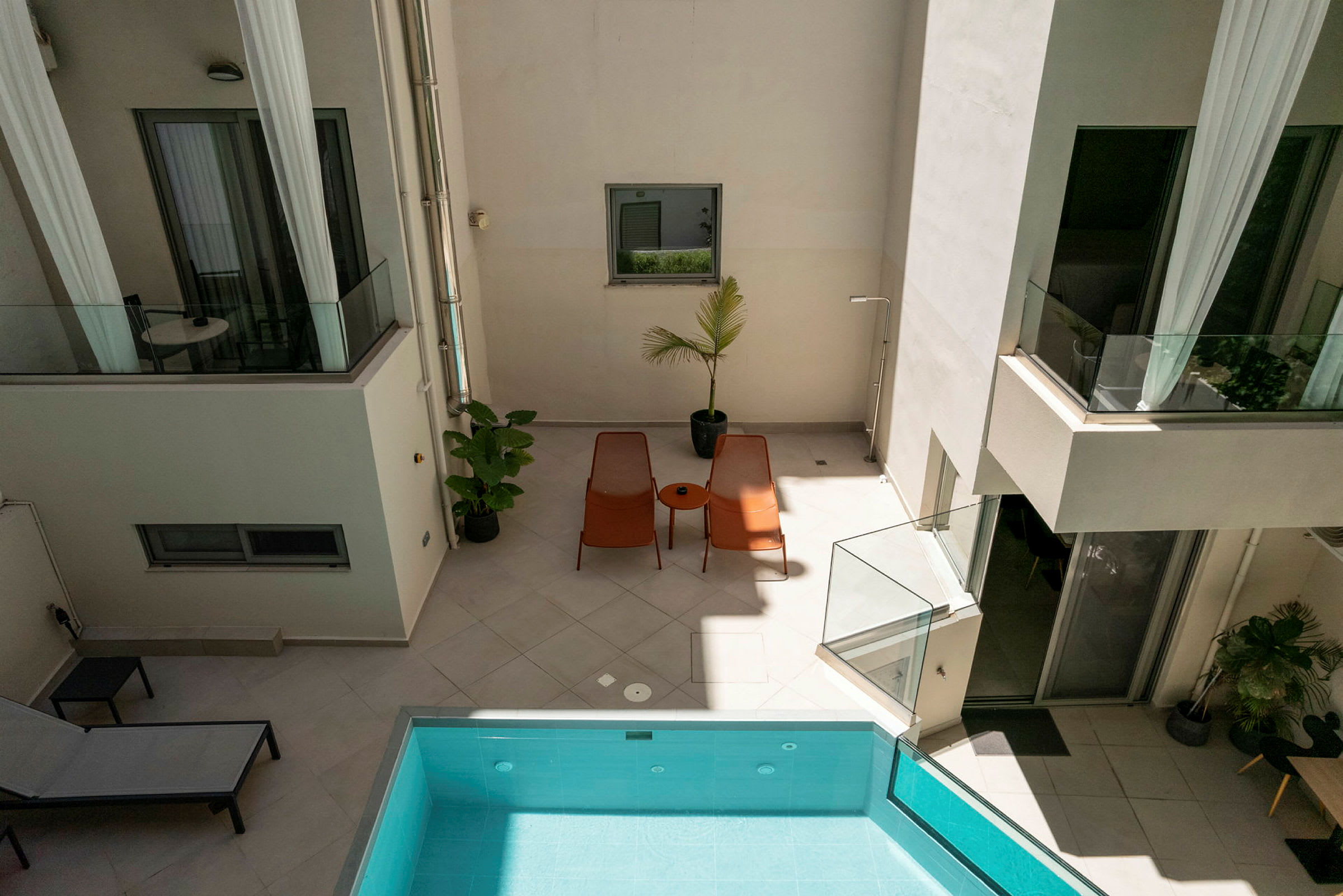 Billede af en indre gårdhave med liggestole, et bord og en pool. Planter og glasrækværk skaber en moderne atmosfære. (AI-genereret tekst)