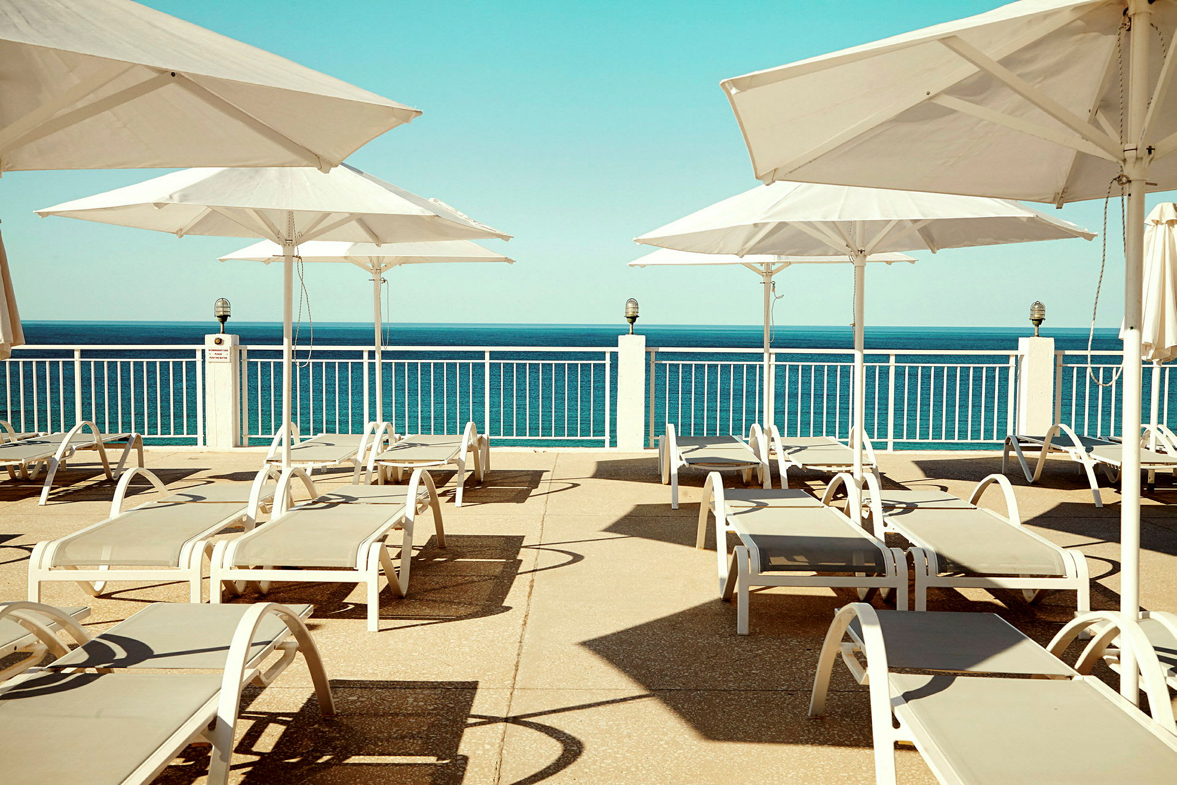 Udsigt over en solterrasse med liggestole og parasoller, med havet i baggrunden. (AI-genereret tekst)