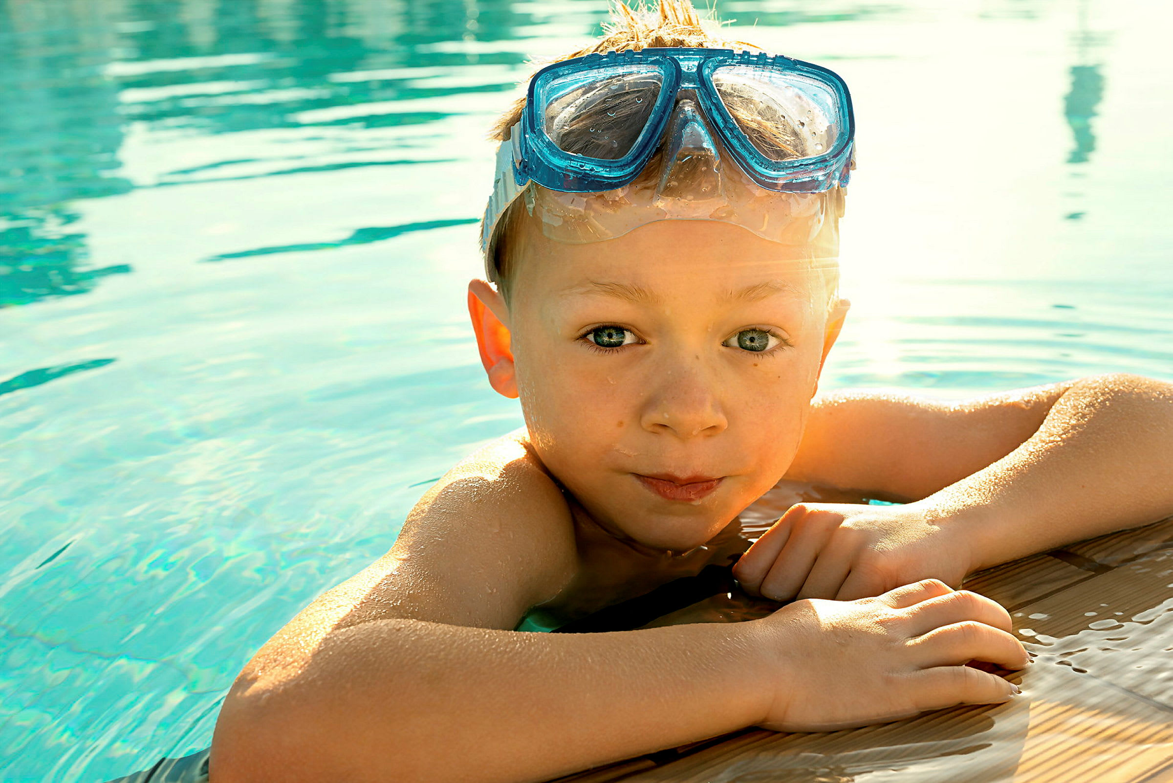 Et barn holder på kanten af en pool og har blå snorkelbriller på. (AI-genereret tekst)