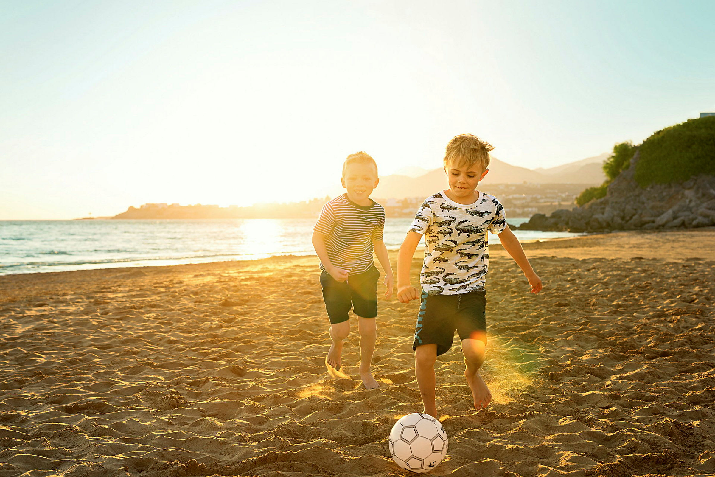 To børn spiller fodbold på en solrig strand. (AI-genereret tekst)