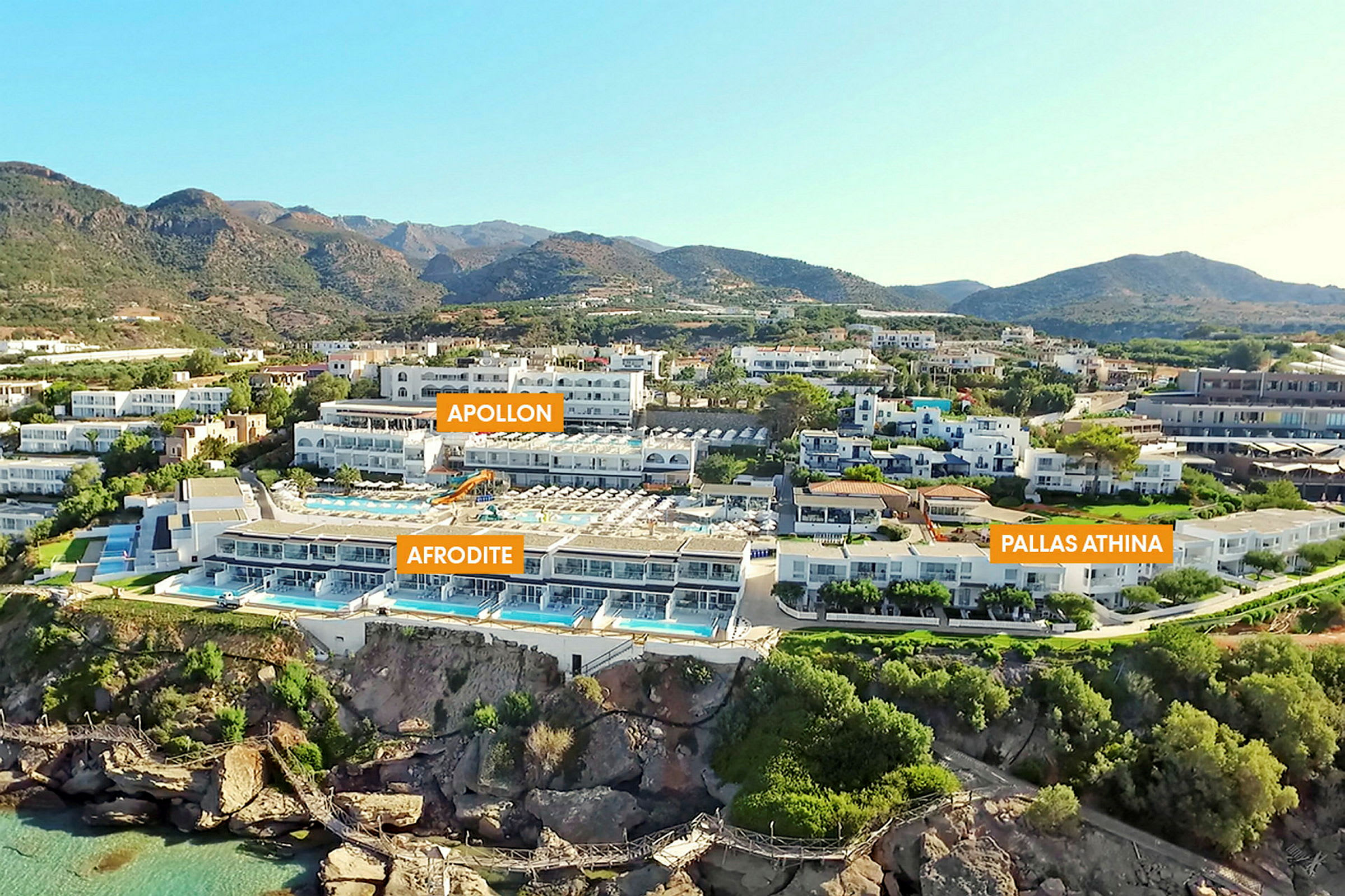 Flere hotelbygninger med pools, omgivet af grønne områder og bjerge. (AI-genereret tekst)