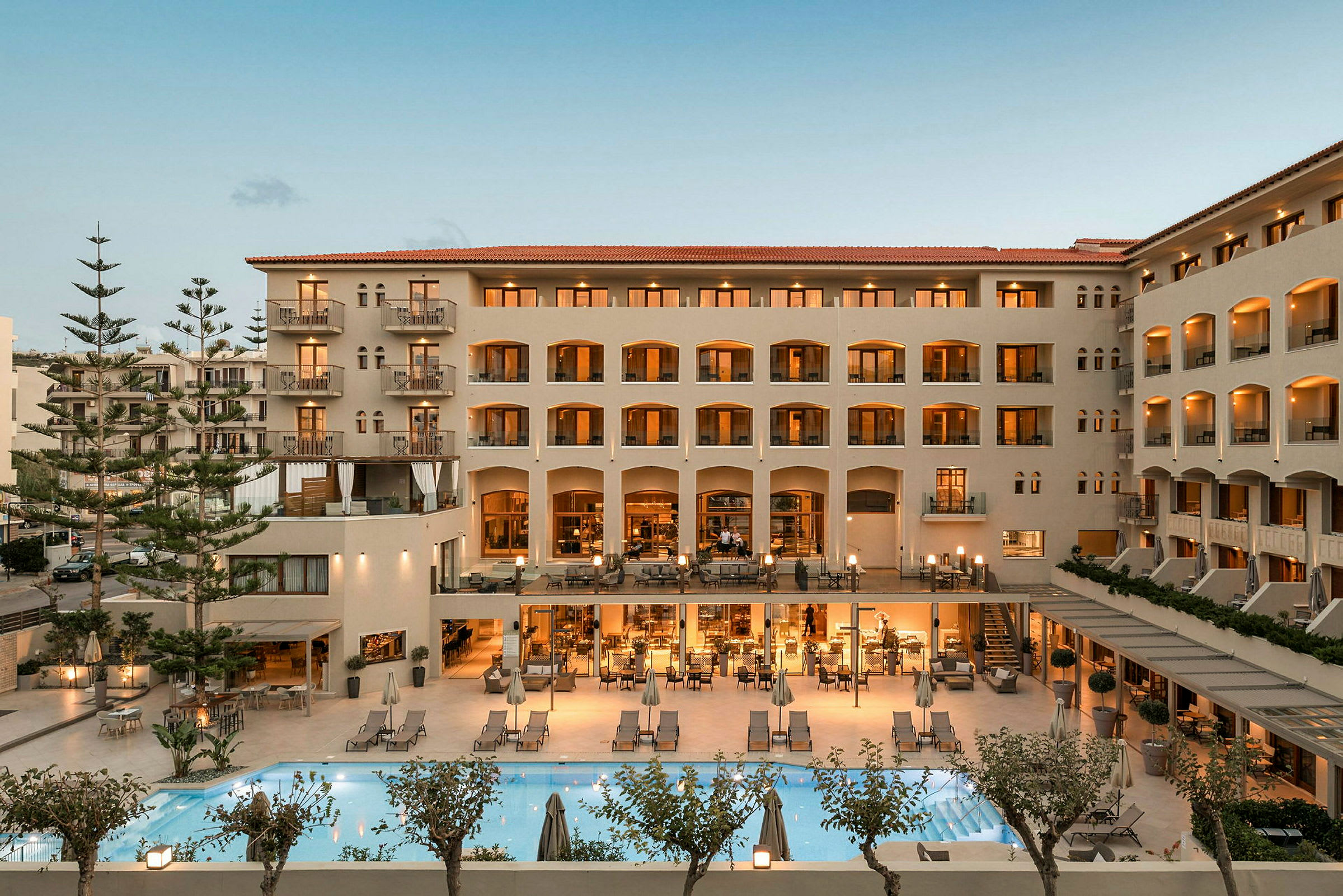 Hotelbygning med oplyste altaner, en udendørs pool og områder med siddepladser. (AI-genereret tekst)