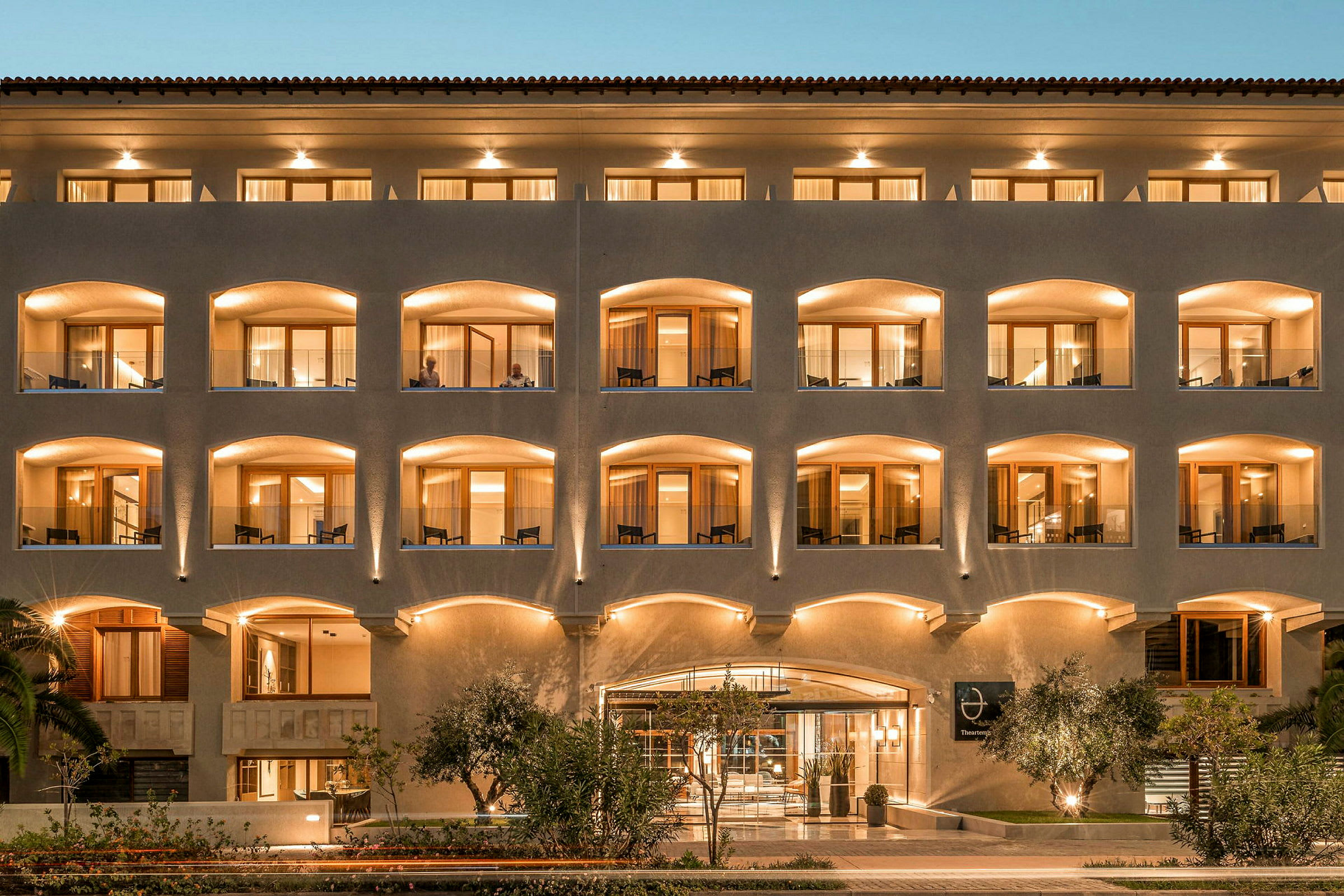 Facade af et hotel med flere etager og oplyste altaner. (AI-genereret tekst)