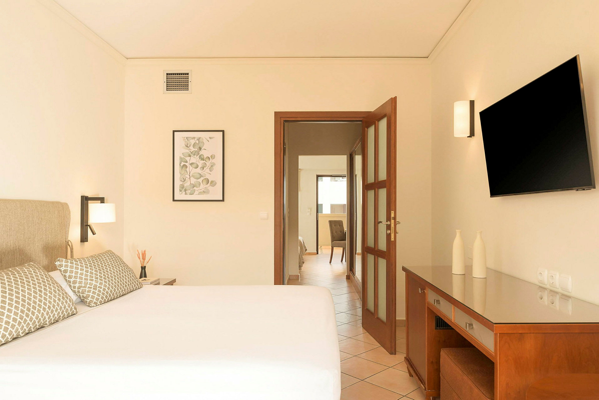 Hotelværelse med en dobbeltseng, sengelamper, en vægmonteret TV og et skrivebord med dekorative genstande. (AI-genereret tekst)