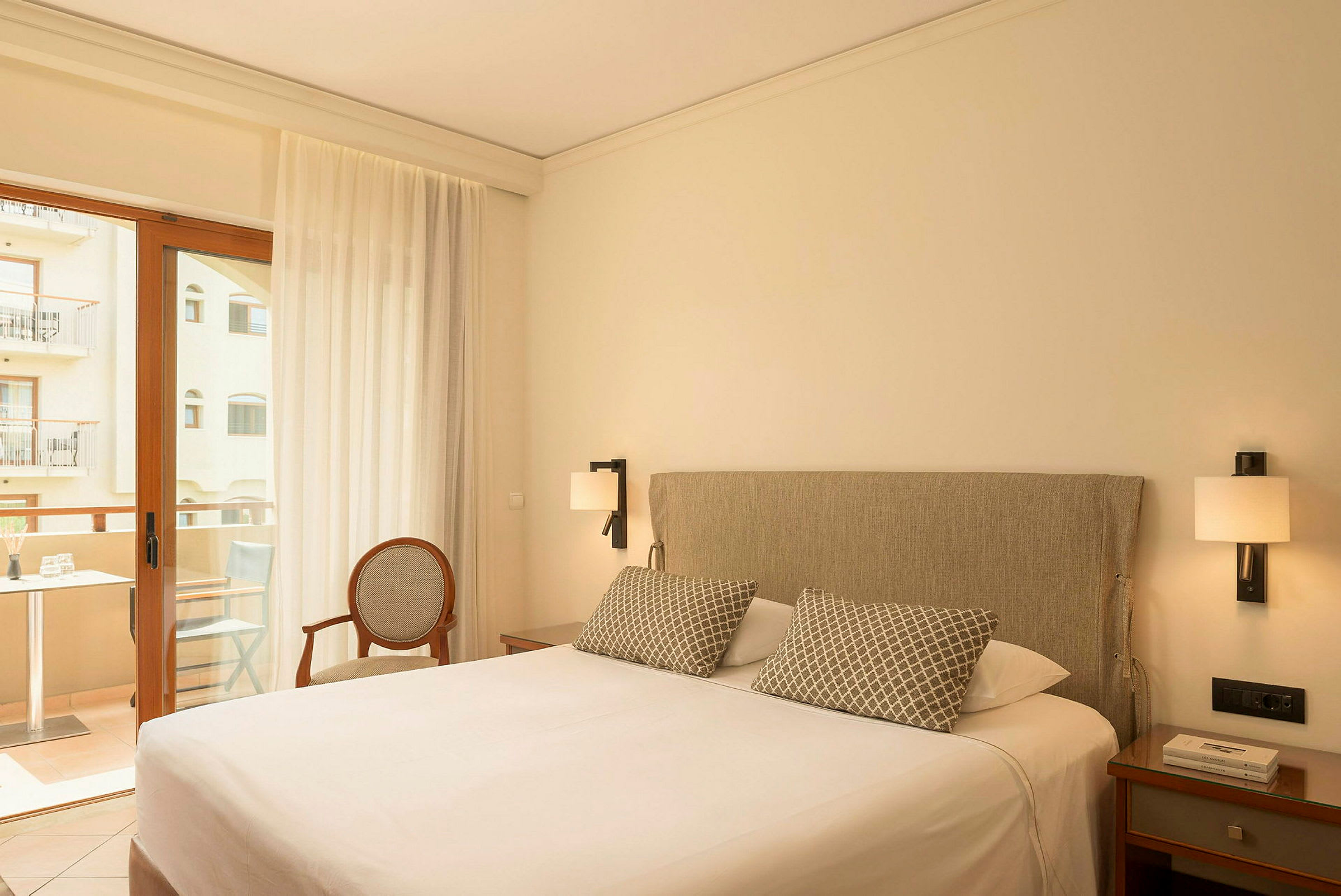 Hotelværelse med en dobbeltseng, natbord, en stol og en altandør med udsigt til en balkon. (AI-genereret tekst)