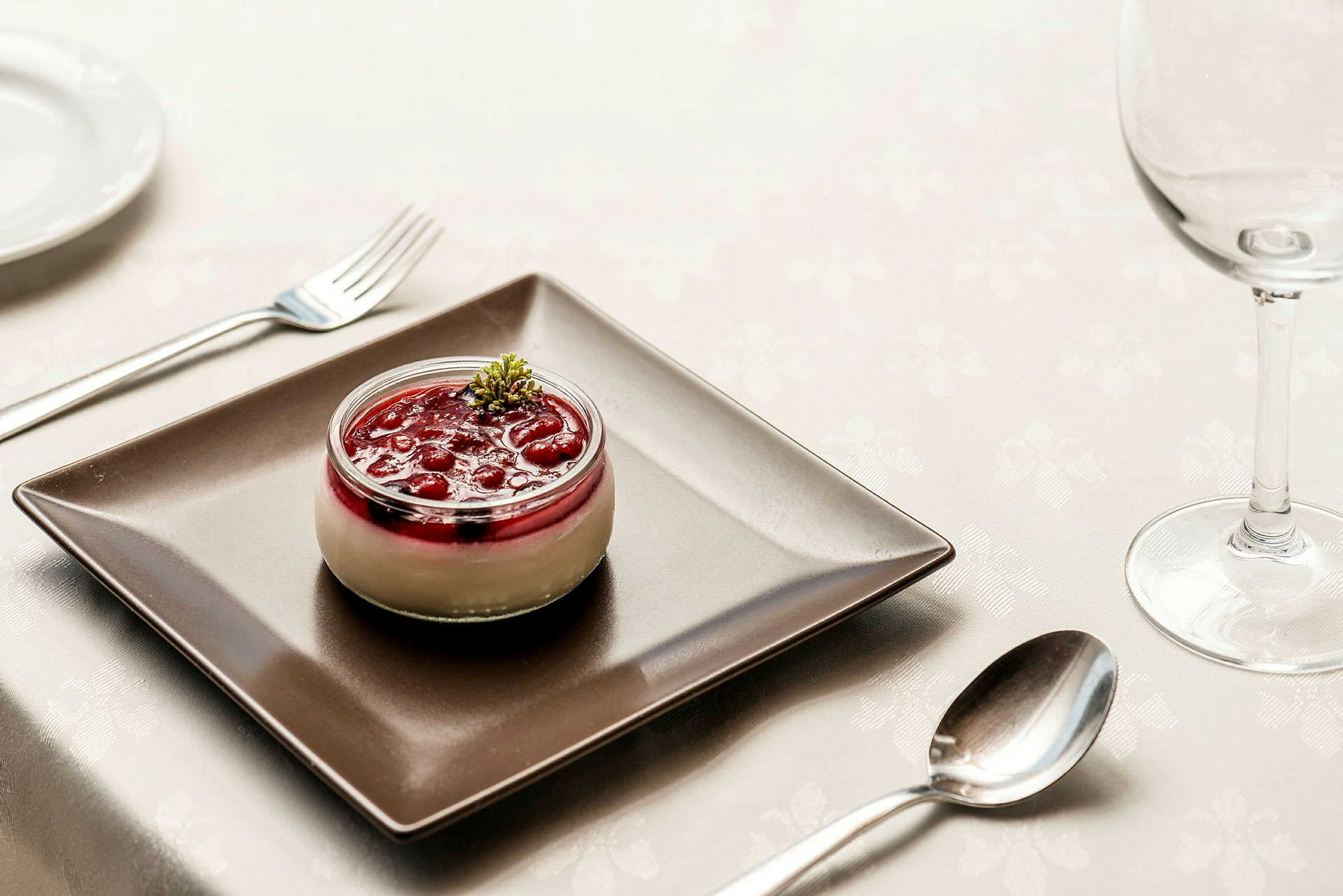 Dessert i glas med røde bær og fløde, serveret på sort tallerken. (AI-genereret tekst)