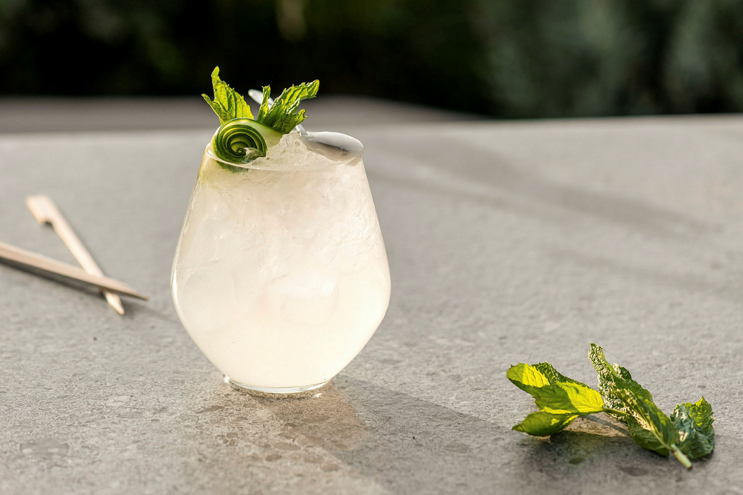Et glas med en kold drink, pyntet med mynte og agurkspiral, står på en bordoverflade. (AI-genereret tekst)