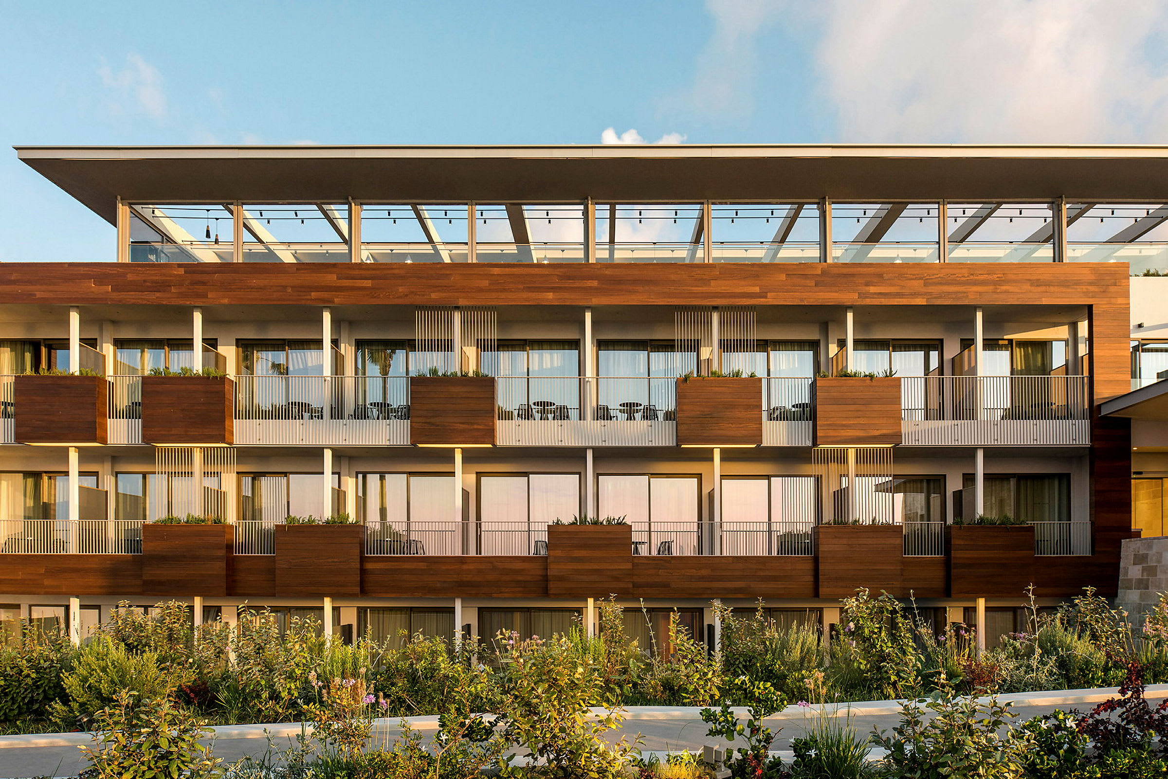 Den moderne facade af et hotel med altaner og beplantning foran. (AI-genereret tekst)