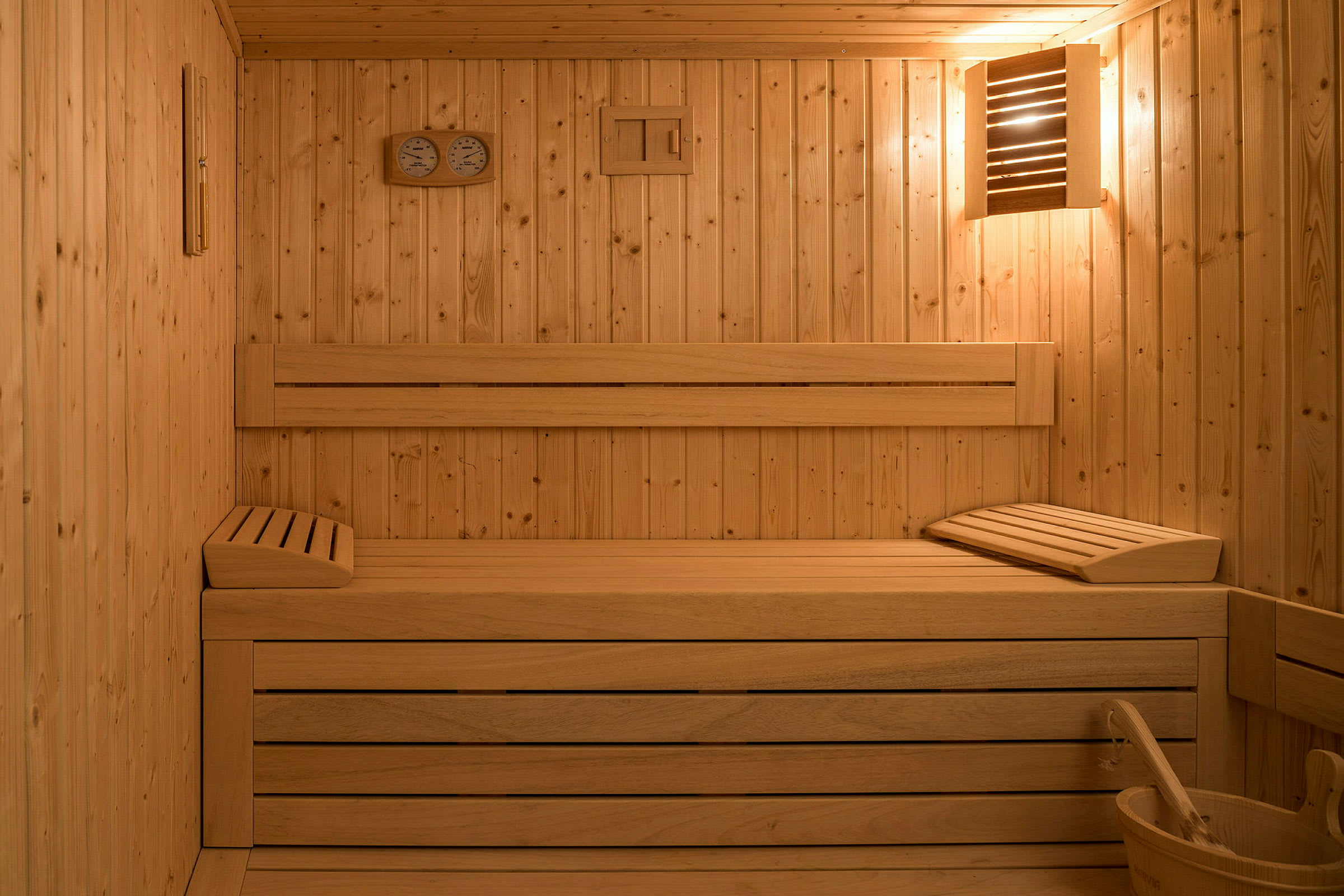 En sauna med trævægge, siddebænke og et bastustermometer. (AI-genereret tekst)