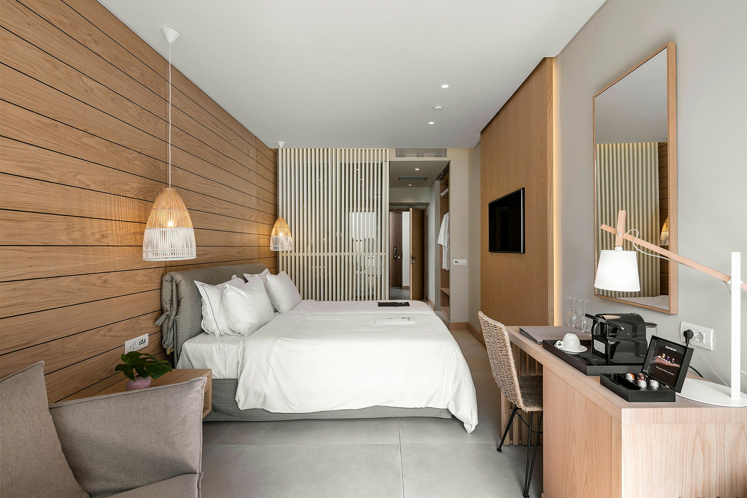 Et lyst og moderne hotelværelse med en stor dobbeltseng, et skrivebord og en dekorativ marmorpanel på væggen. (AI-genereret tekst)