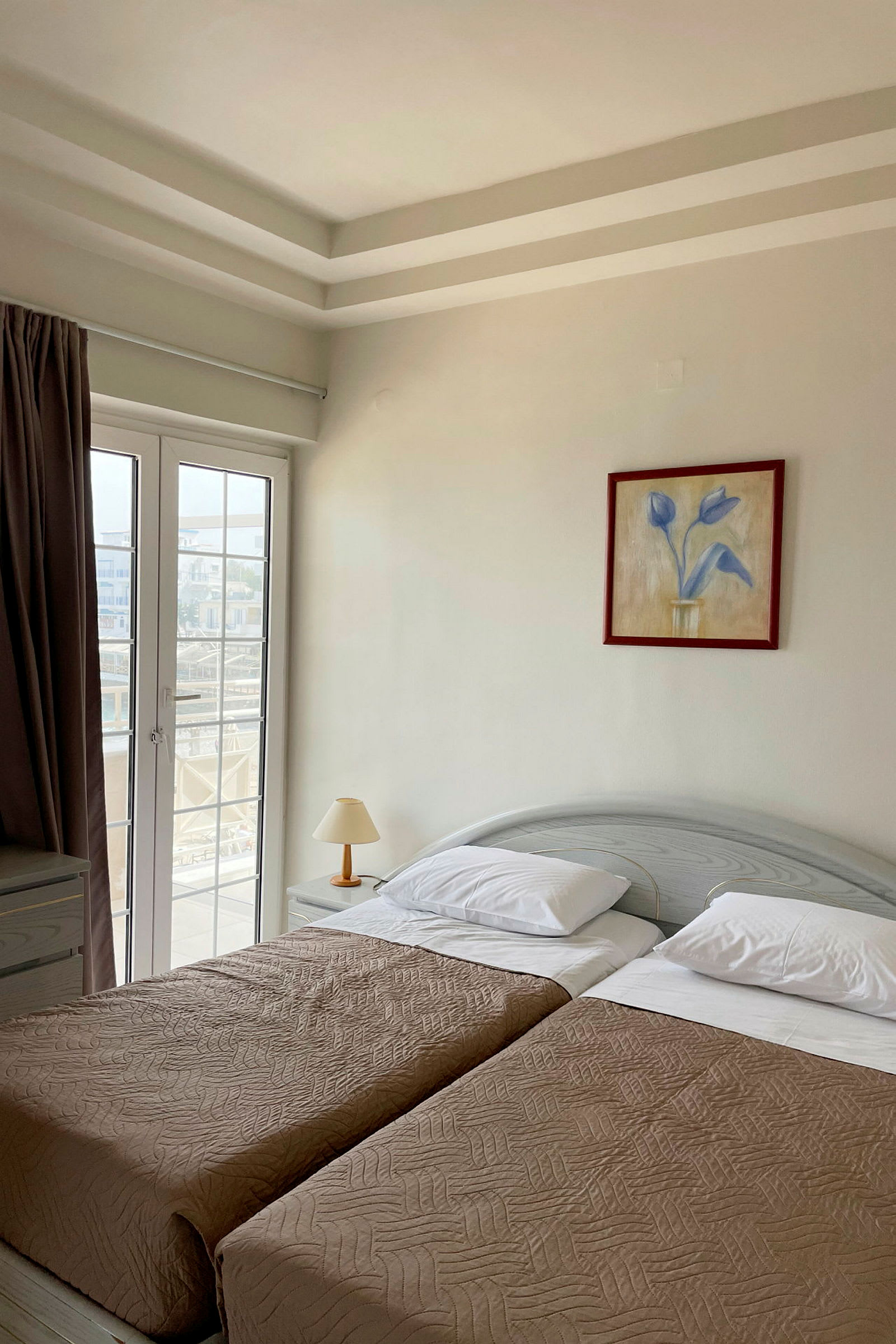 Et hotelværelse med to enkeltsenge, en lampe og en glasdør. (AI-genereret tekst)