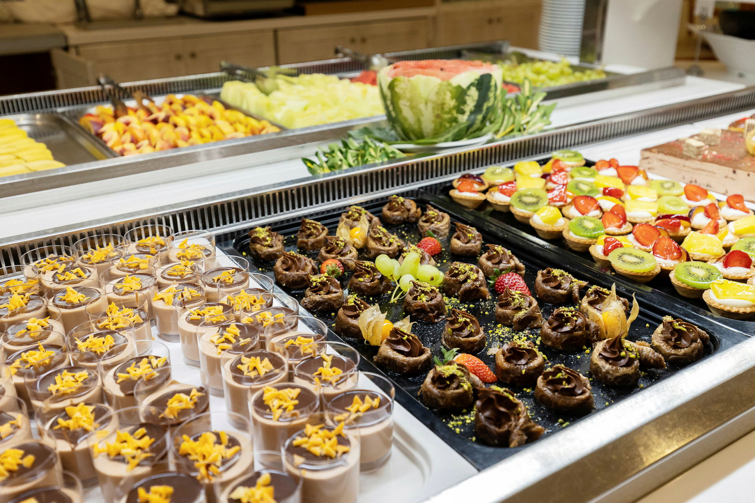 Buffet med forskellige desserter, inklusive chokolademousse, frugtdekorationer og små tærter. (AI-genereret tekst)